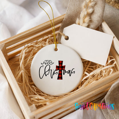 A white ceramic ornament with a red and black plaid design and the text "Merry Christmas" is displayed in a wooden crate, surrounded by straw.