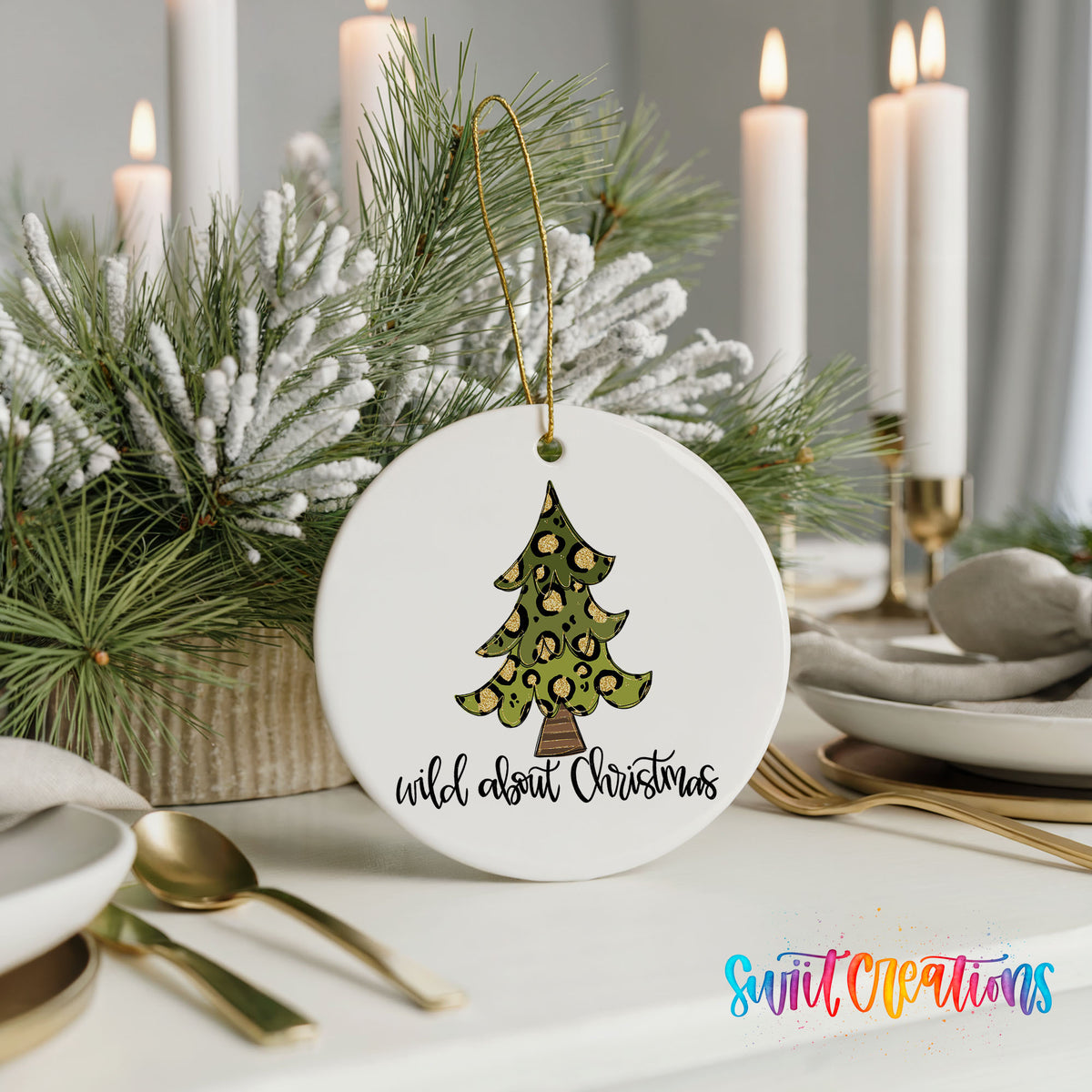 A white Christmas ornament with a leopard print tree design, placed on a table with candles and a floral arrangement.