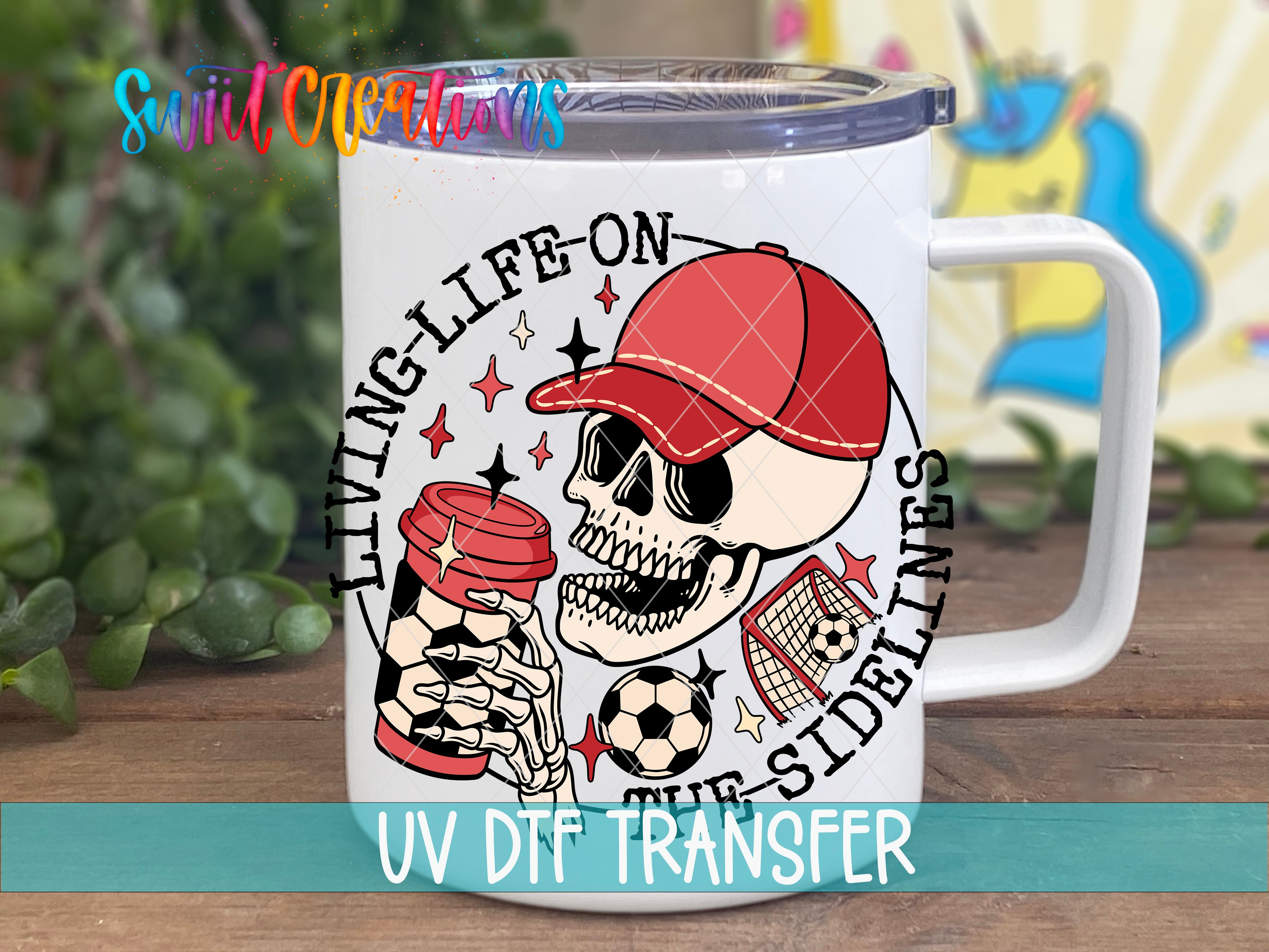 A white mug with a skull and soccer ball design, along with the text "LIVING LIFE ON THE SIDELINES" and "UV DDF TRANSFER".