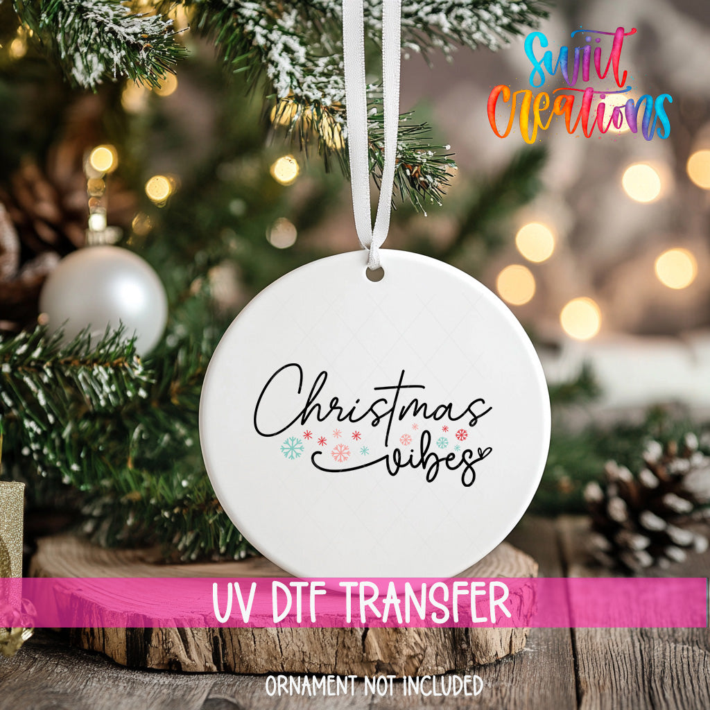 A white Christmas ornament with the text "Christmas vibes" printed on it, hanging from a tree branch.