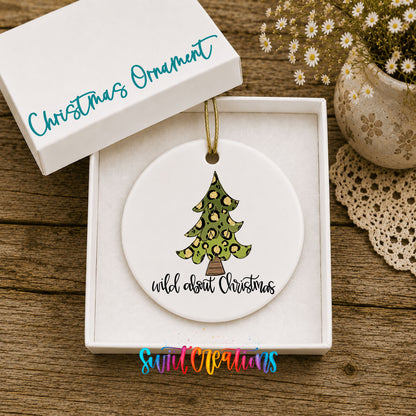 A white Christmas ornament with a leopard print design is displayed in a white box, accompanied by a small potted plant and a lace doily on a wooden surface.