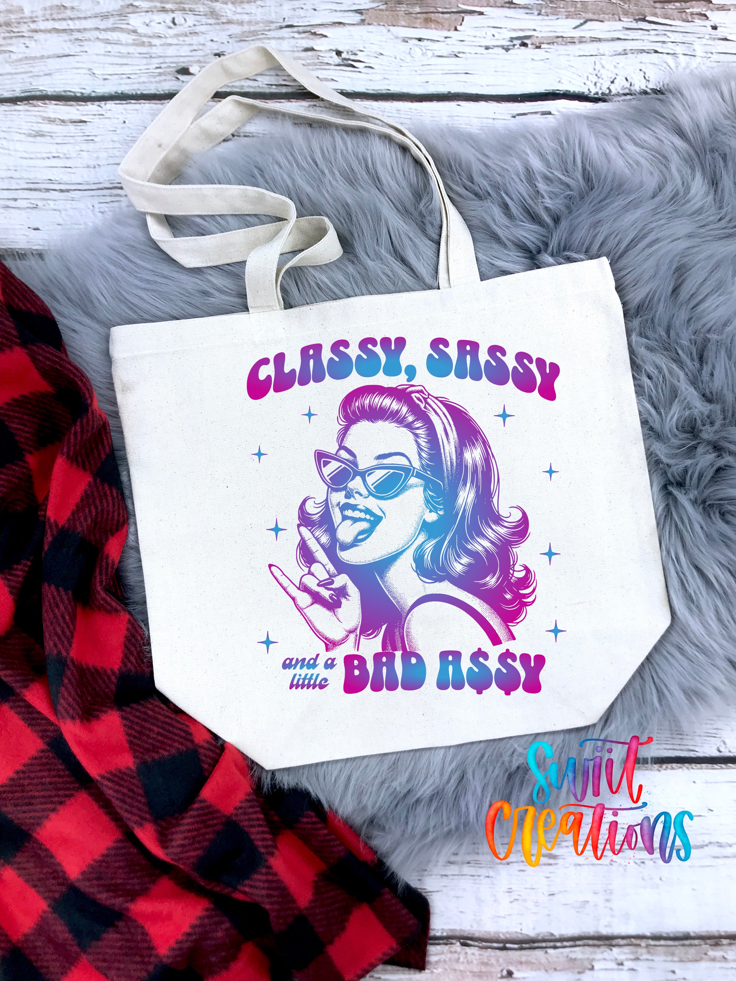 A white tote bag with a colorful graphic design featuring a woman's face wearing sunglasses and the text "CLASSY, SASSY and a little BAD ASSY" printed on it.