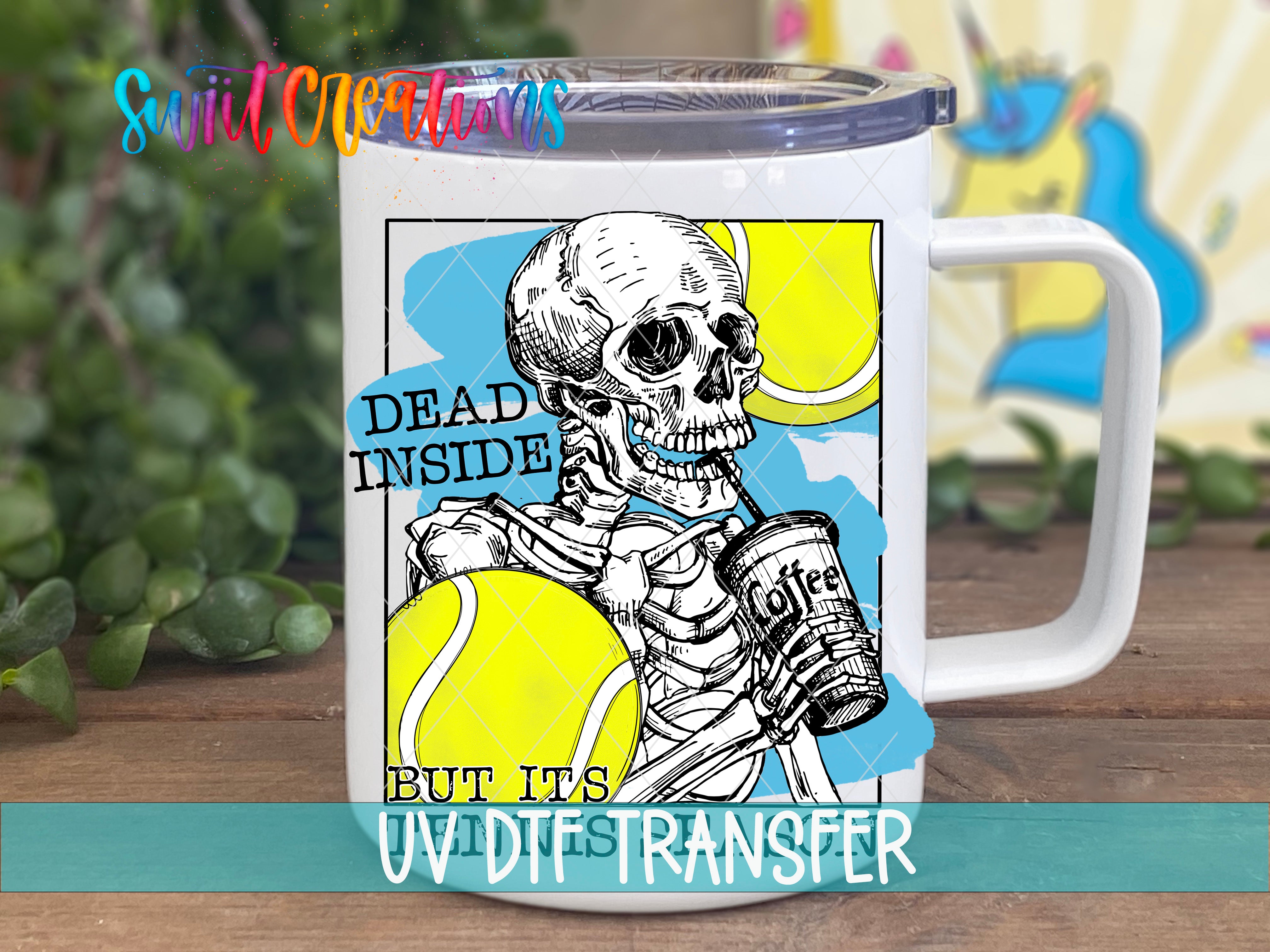 A white mug with a printed design featuring a skeleton holding a can of coffee and tennis balls, along with the text "DEAD INSIDE" and "BUT IT'S UV DESTINER".