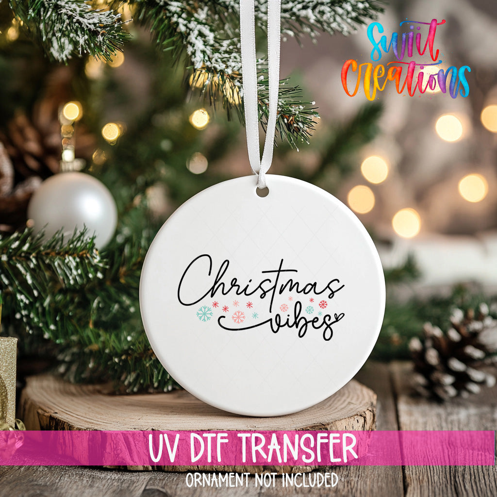 A white Christmas ornament with the text "Christmas vibes" printed on it, hanging from a tree branch.