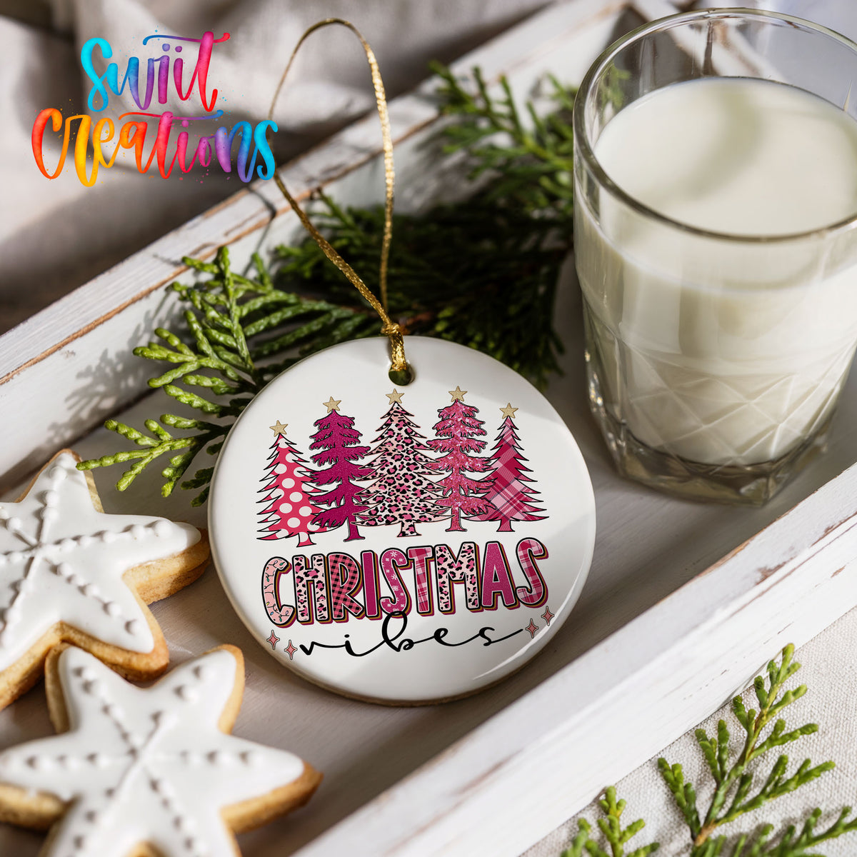 a Christmas ornament with a tree design, a glass of milk, and some cookies on a white tray.