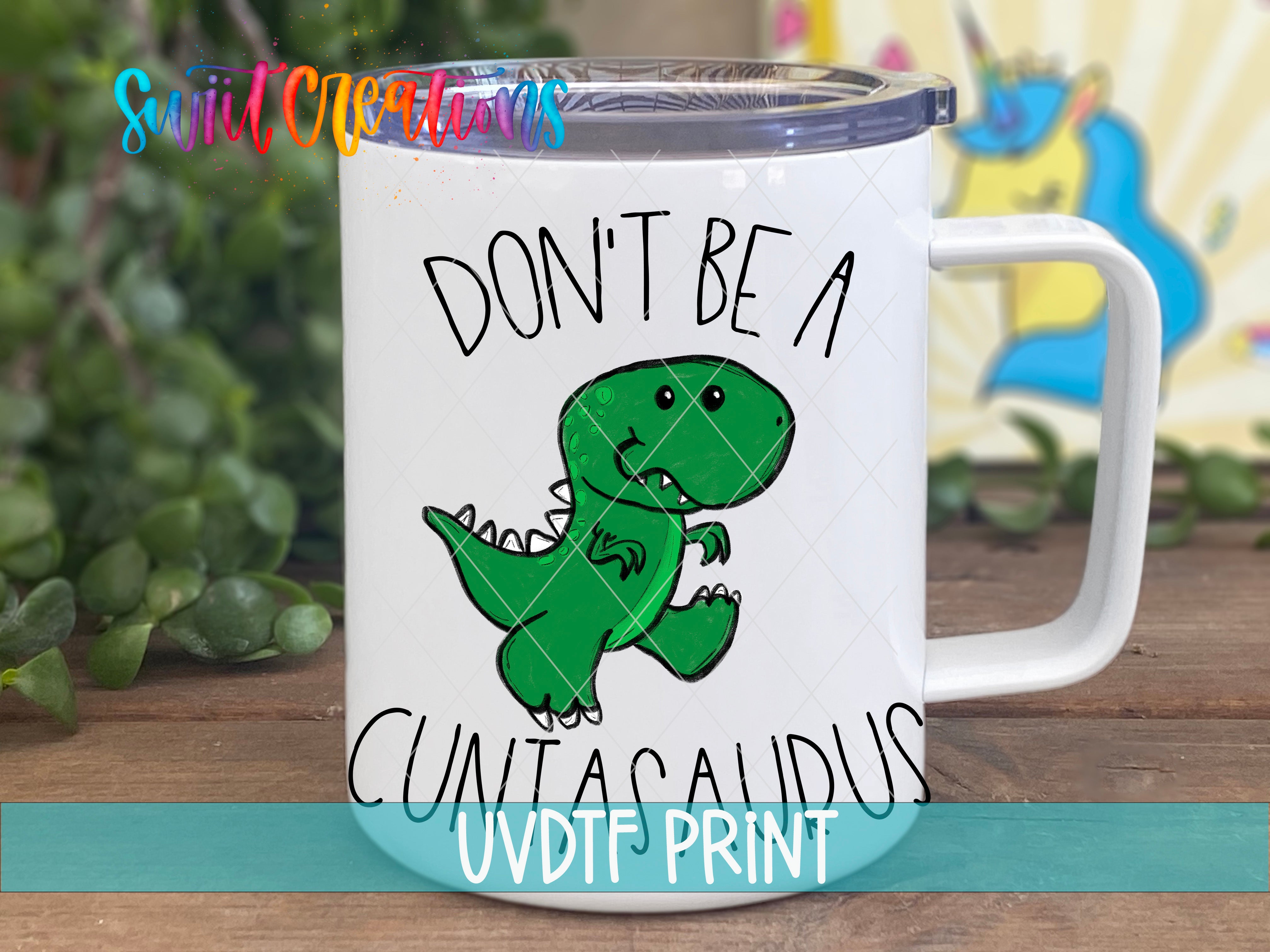 A white mug with a cartoon dinosaur and the text "DON'T BE A CUNTA CURIUS" printed on it.