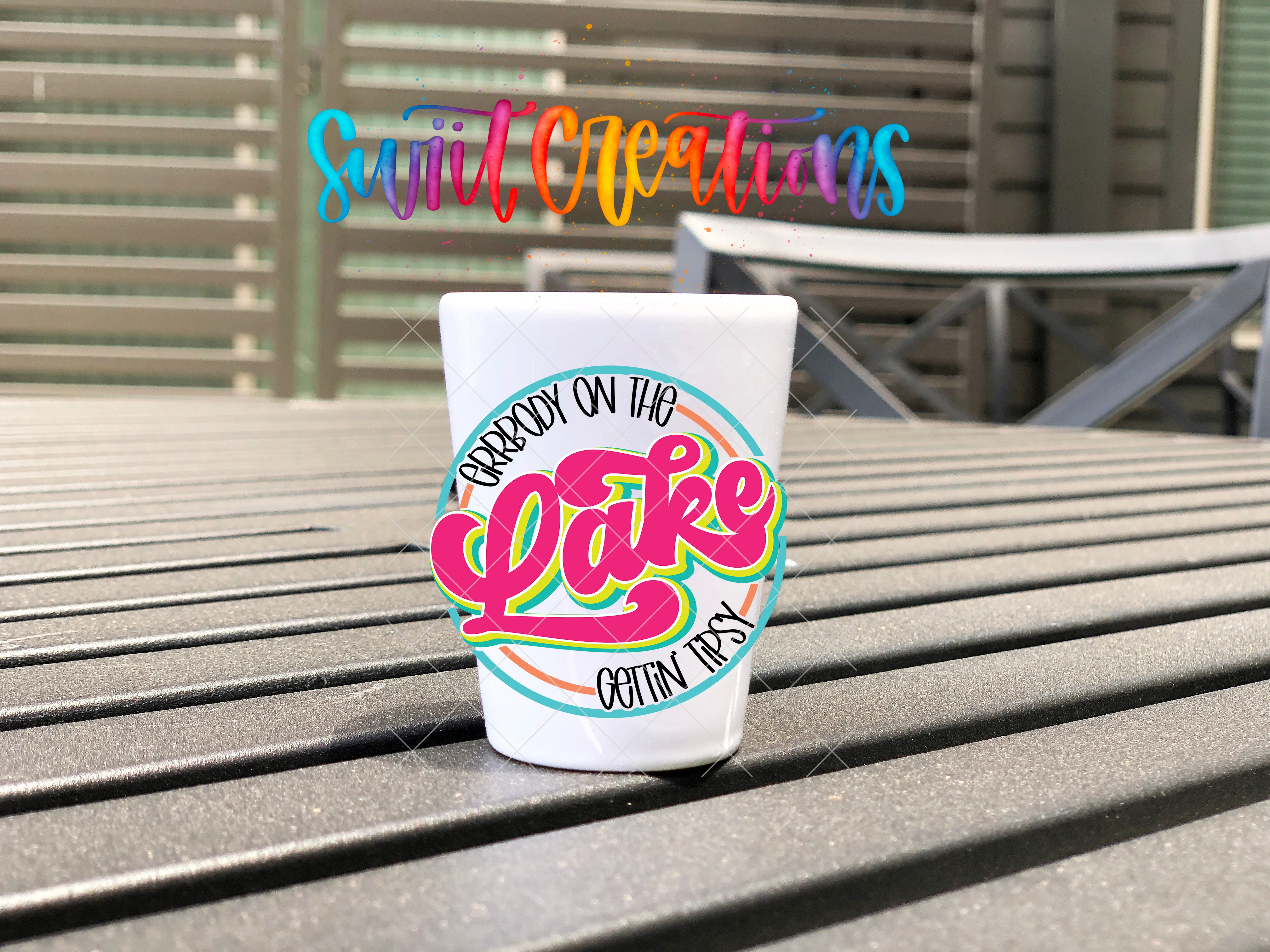A white shot glass with a colorful graphic and text on it, placed on a wooden surface.