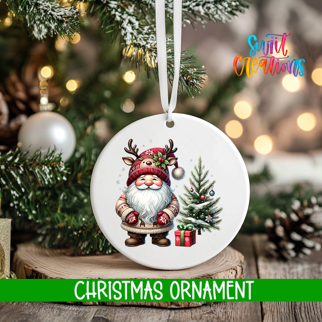 A white Christmas ornament featuring a smiling Santa Claus wearing a red hat and holding a gift box, with a Christmas tree and pine cones in the background.