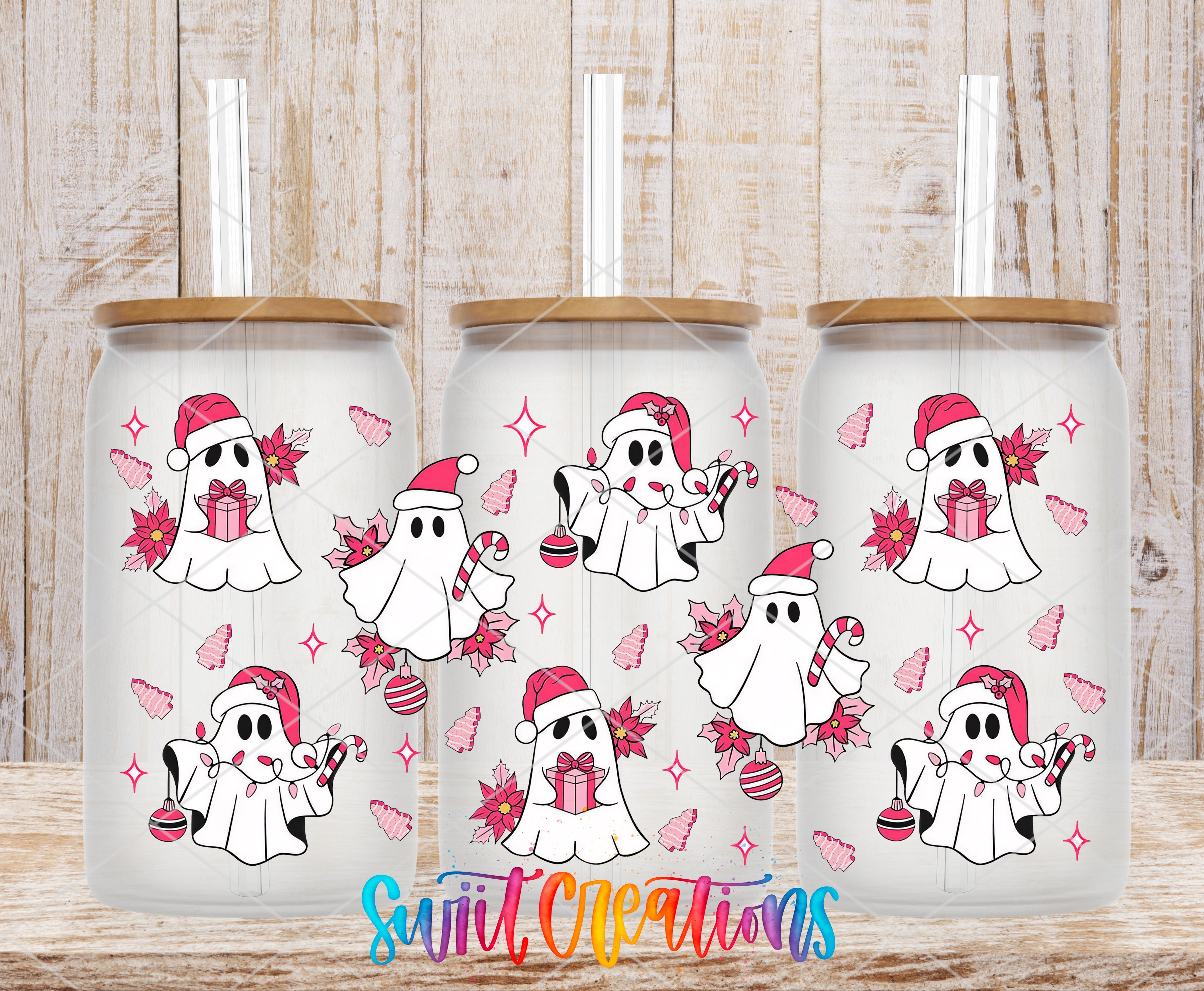 three glass tumblers with a festive design of pink ghost characters and Christmas-themed elements, such as presents and ornaments, on a wooden background.