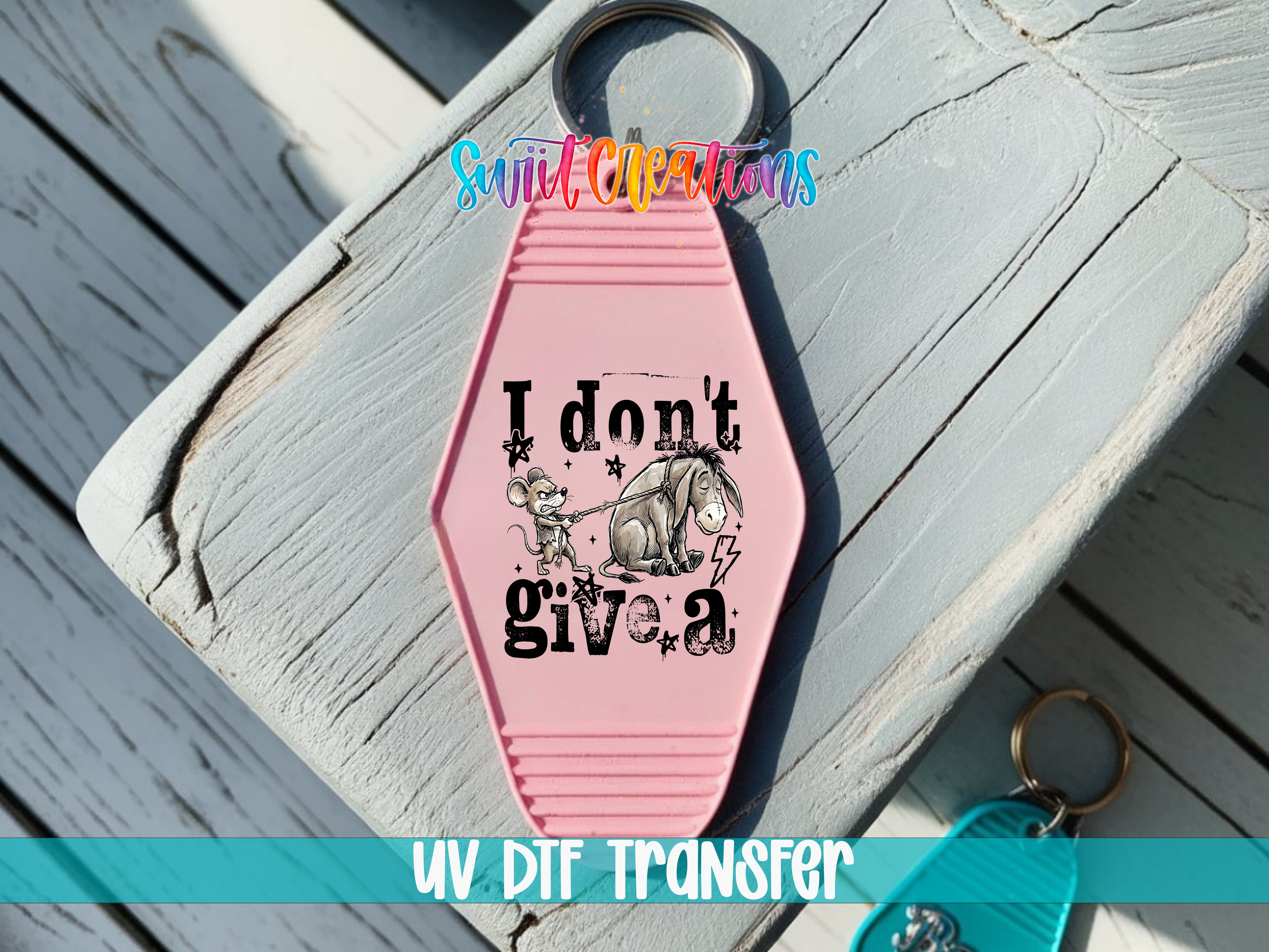 A pink keychain with a cartoon image of a mouse and the text "I don't give a" printed on it, placed on a wooden surface.