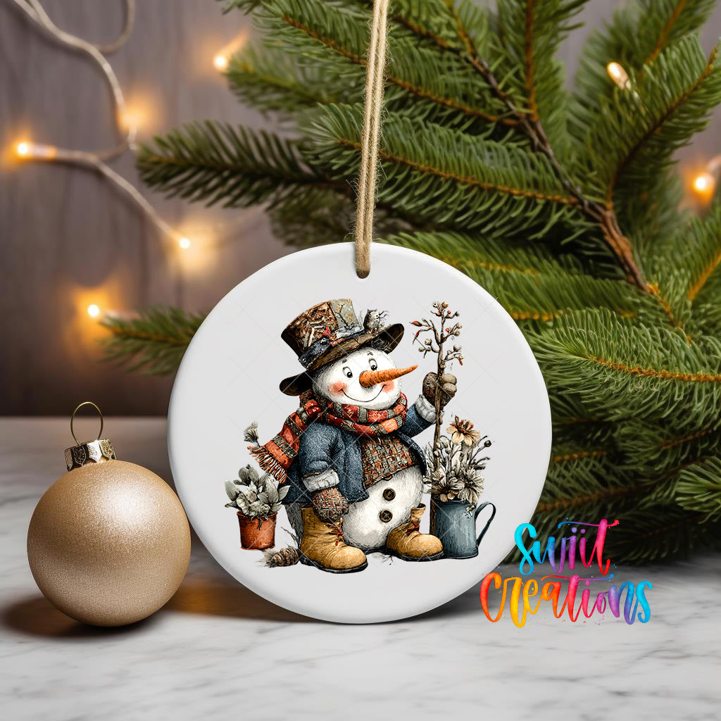 A white ceramic ornament featuring a snowman is displayed on a table, with a Christmas tree and a gold ornament visible in the background.