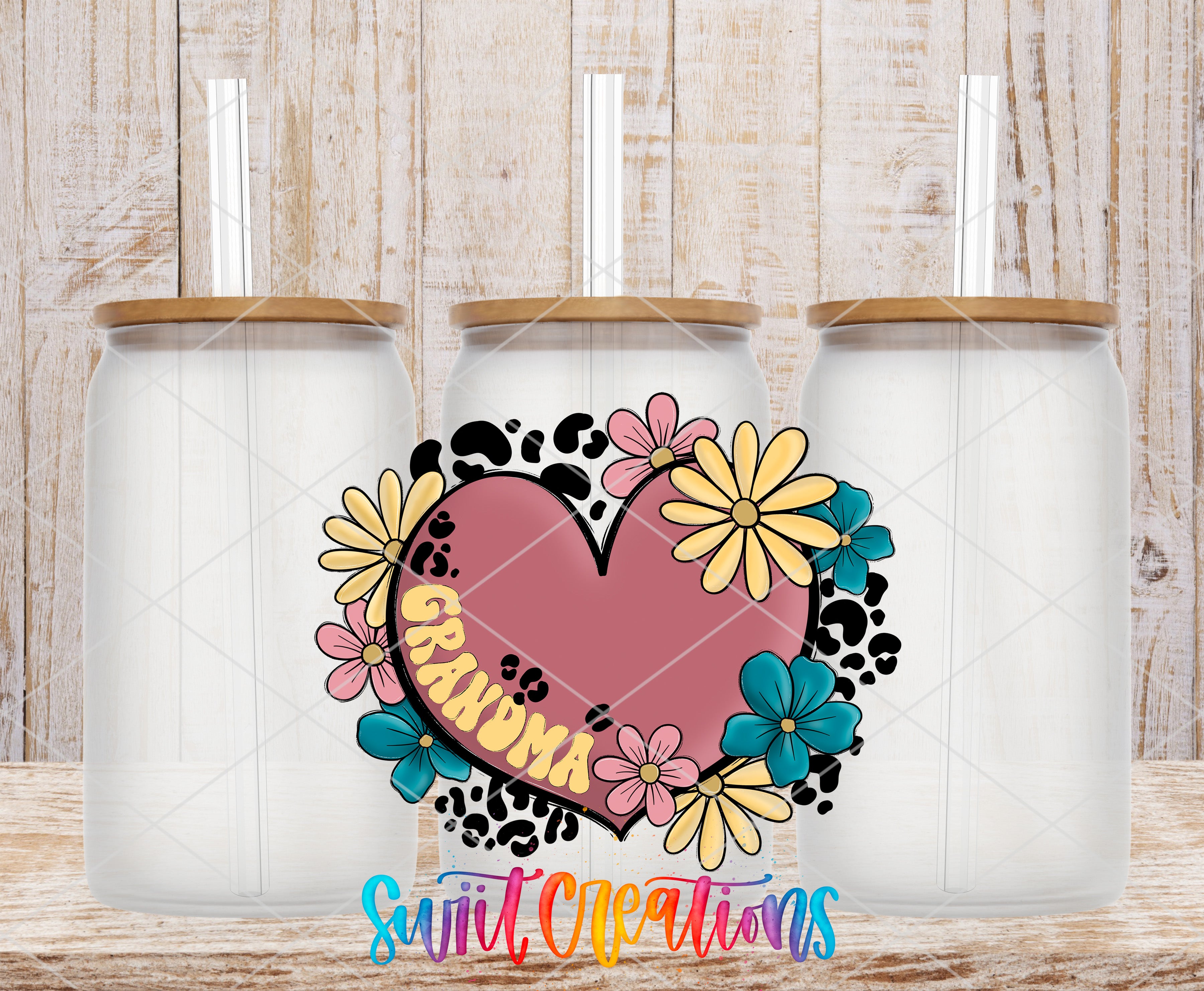 three glass jars with lids, each containing a straw, arranged in a row against a wooden background. The jars are decorated with a colorful floral design, including a heart-shaped element with the word "GRANDMA" written on it.