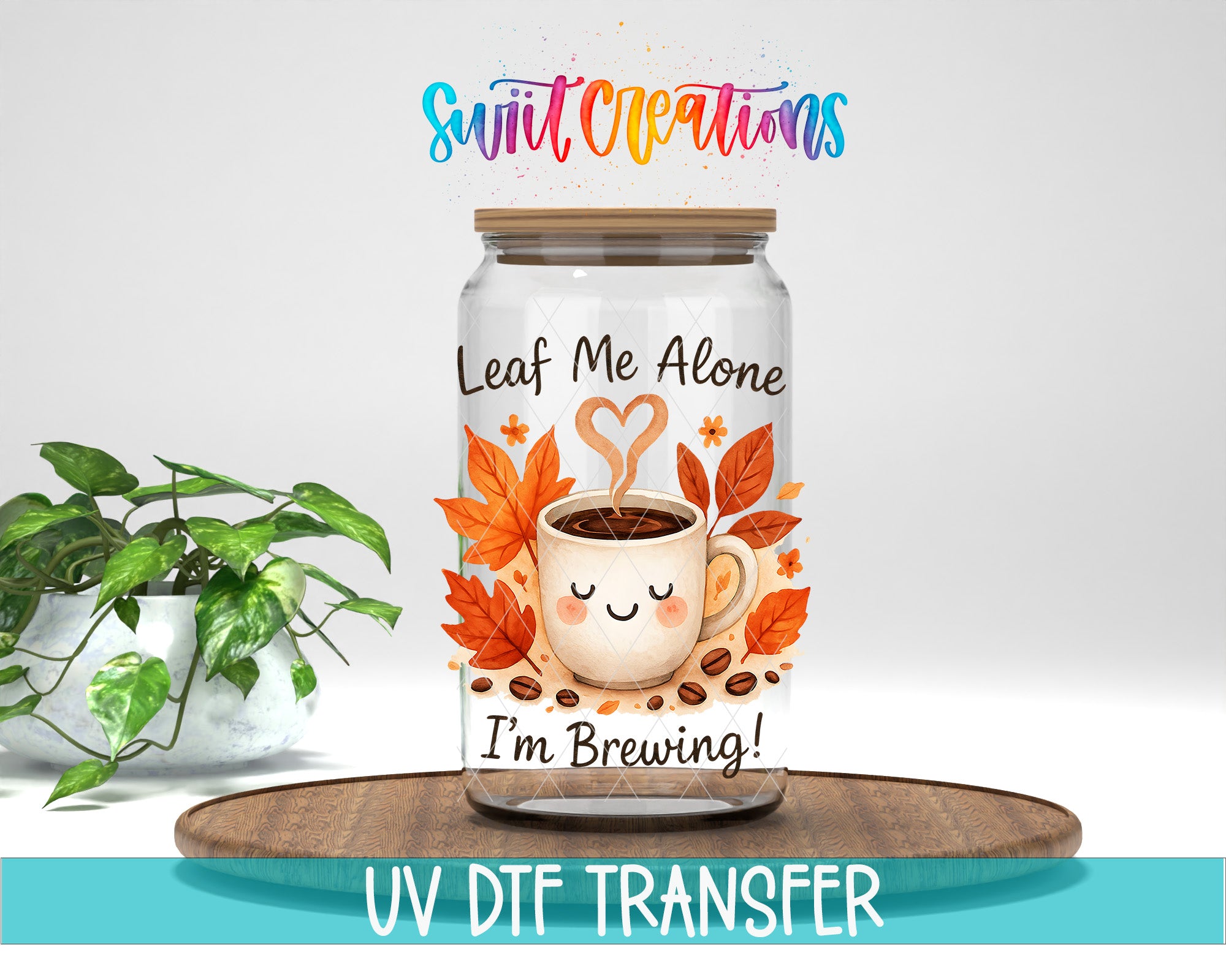 A glass jar with a coffee cup design and autumn leaves, accompanied by the text "Leaf Me Alone I'm Brewing!" and "Swift Creations". The jar is placed on a wooden surface, and there is a potted plant in the background.