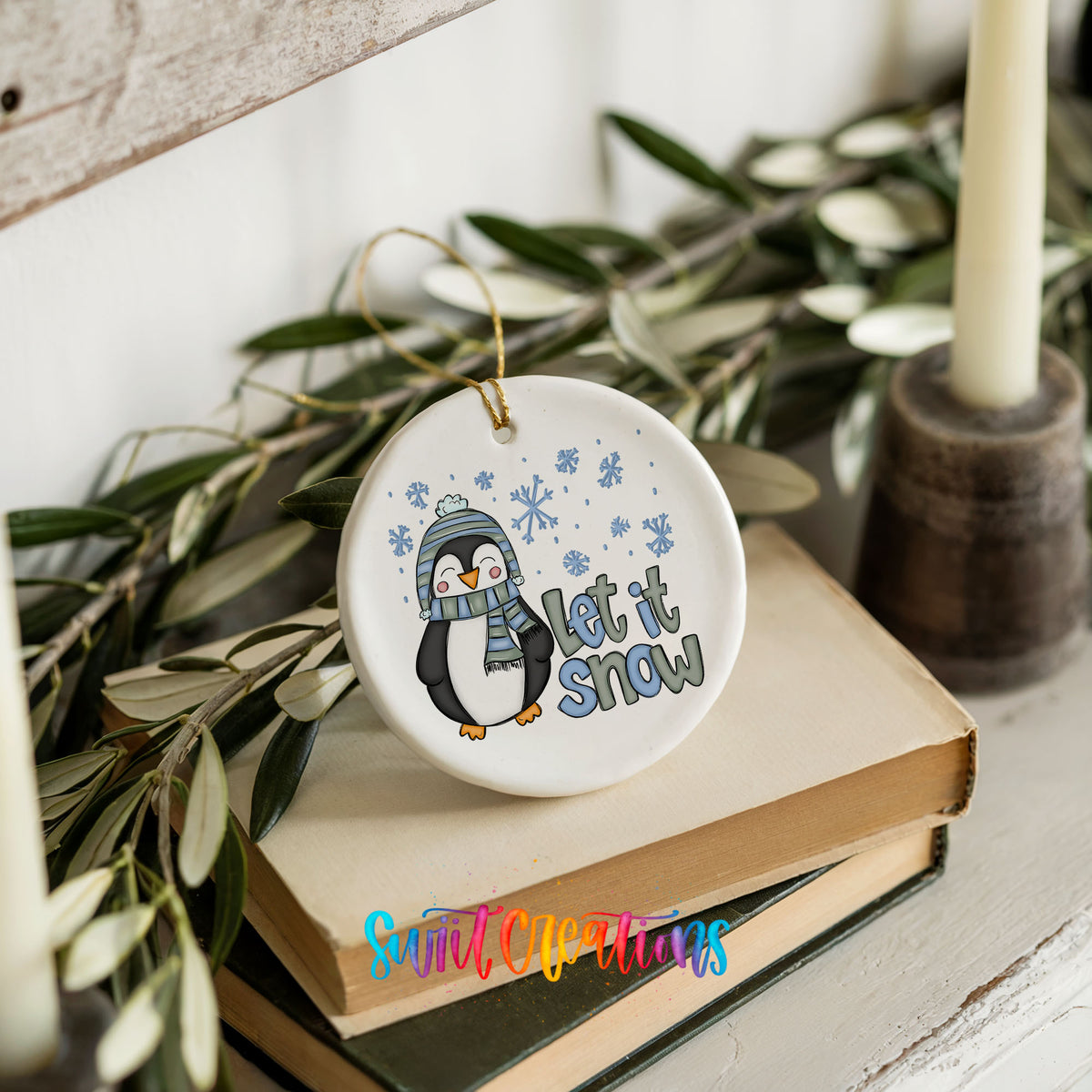 A white ceramic ornament with a penguin and snowflakes, along with the text "Let it snow" is displayed on top of a stack of books.