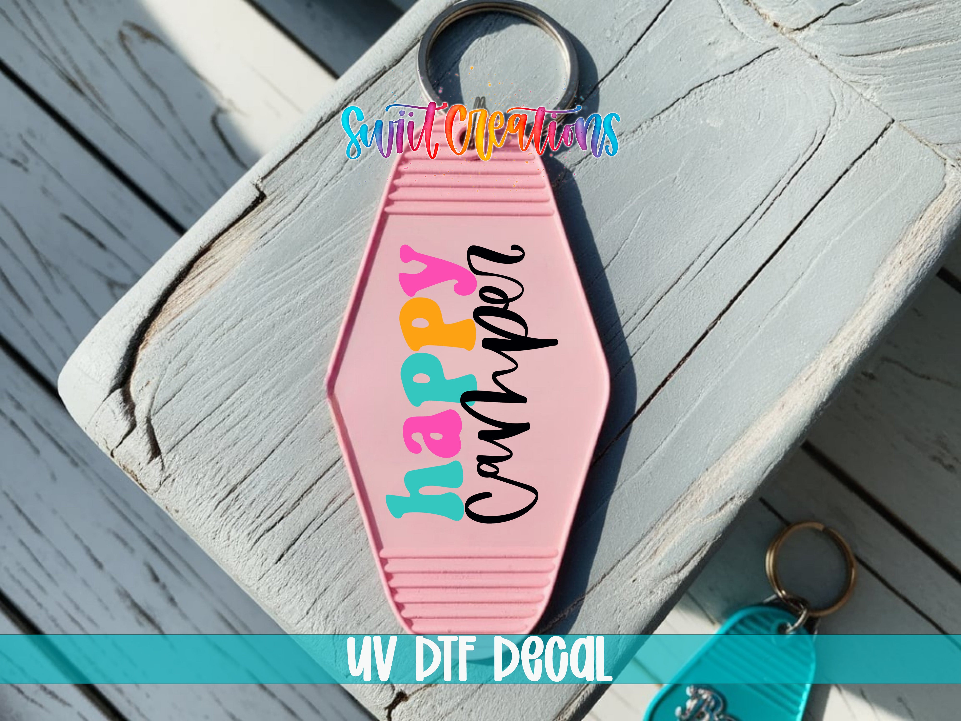 A pink keychain with the text "happyp camp" printed on it, placed on a wooden surface.
