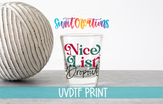 a shot glass with text on it, placed next to a ball of yarn on a table.