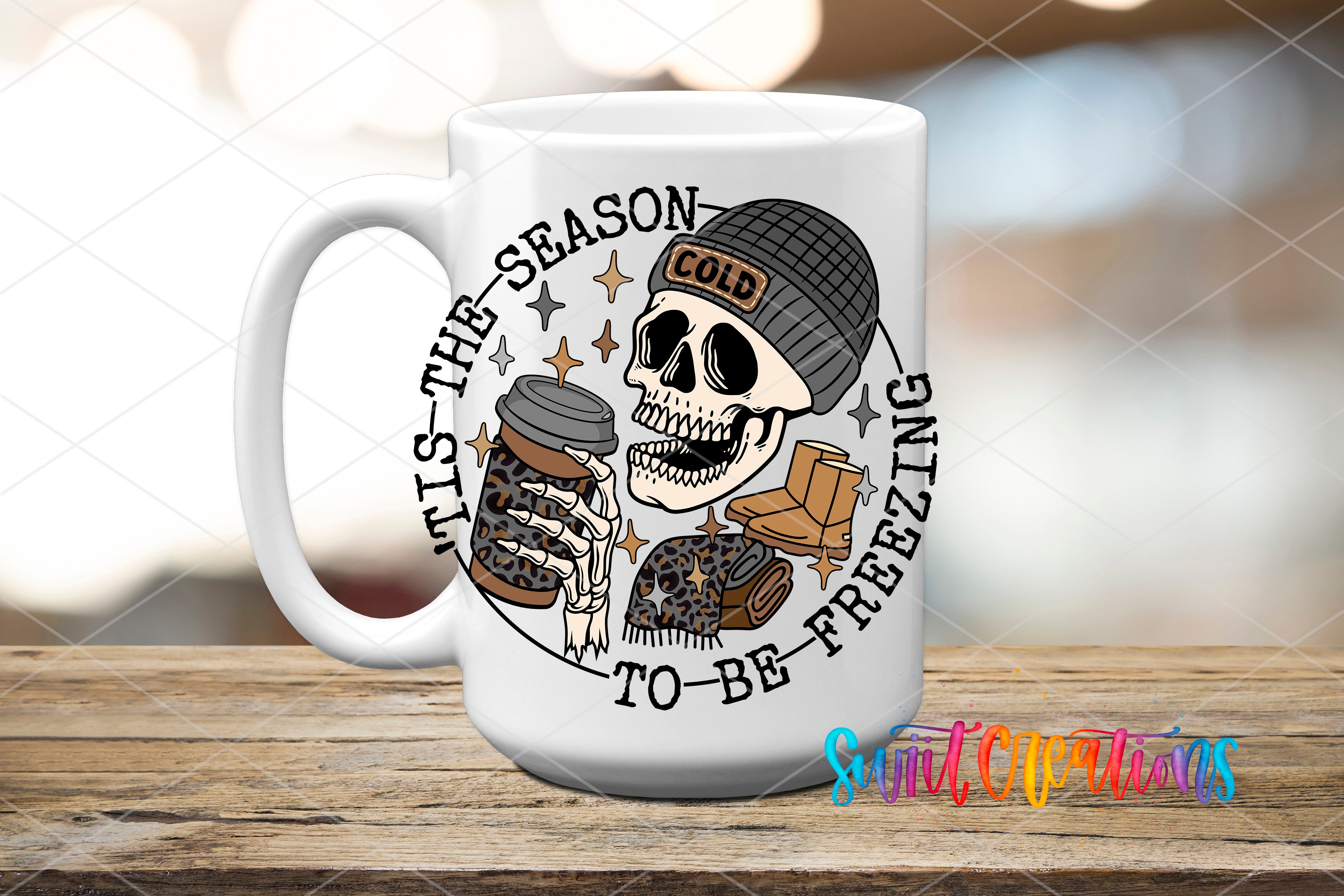 A white ceramic mug with a graphic design featuring a skull wearing a beanie and holding a coffee cup, surrounded by text that reads "It's the season to be freezing".