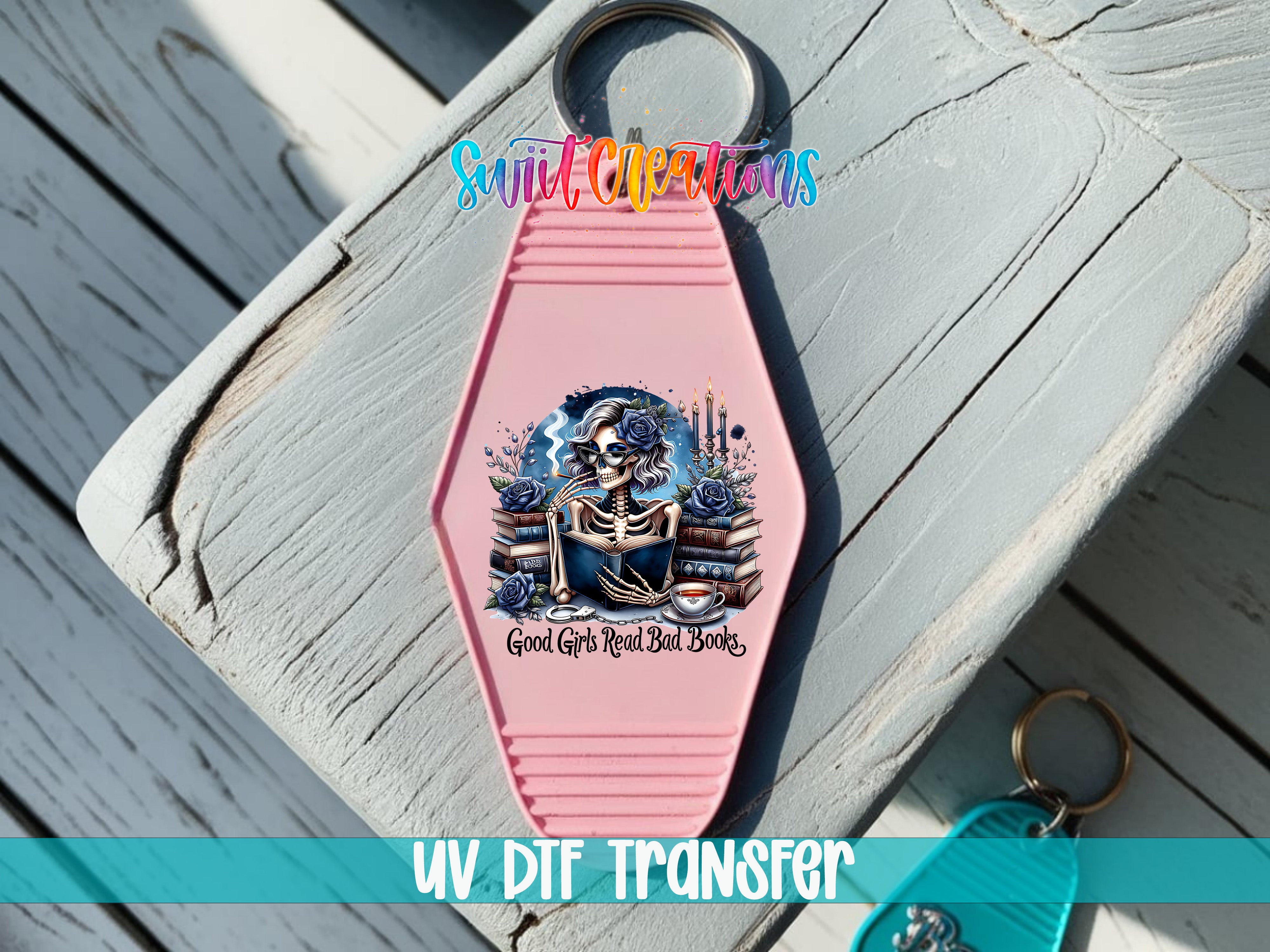 A pink keychain with a skull and crossbones design, along with the text "Good Girls Read Bad Books" printed on it.
