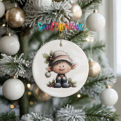 A ceramic ornament featuring a cartoon elf is hanging on a Christmas tree, surrounded by white and gold ornaments.