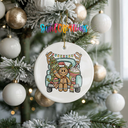 A white Christmas ornament with a gingerbread man and a truck is hanging on a decorated tree.