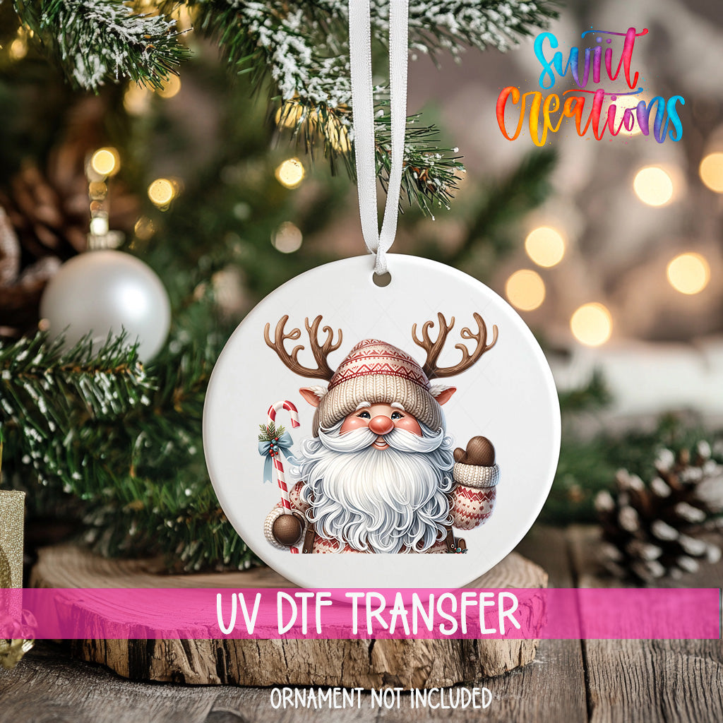 A white ornament with a Santa Claus face and antlers is hanging on a Christmas tree, with a blurred background of pine branches and twinkling lights.