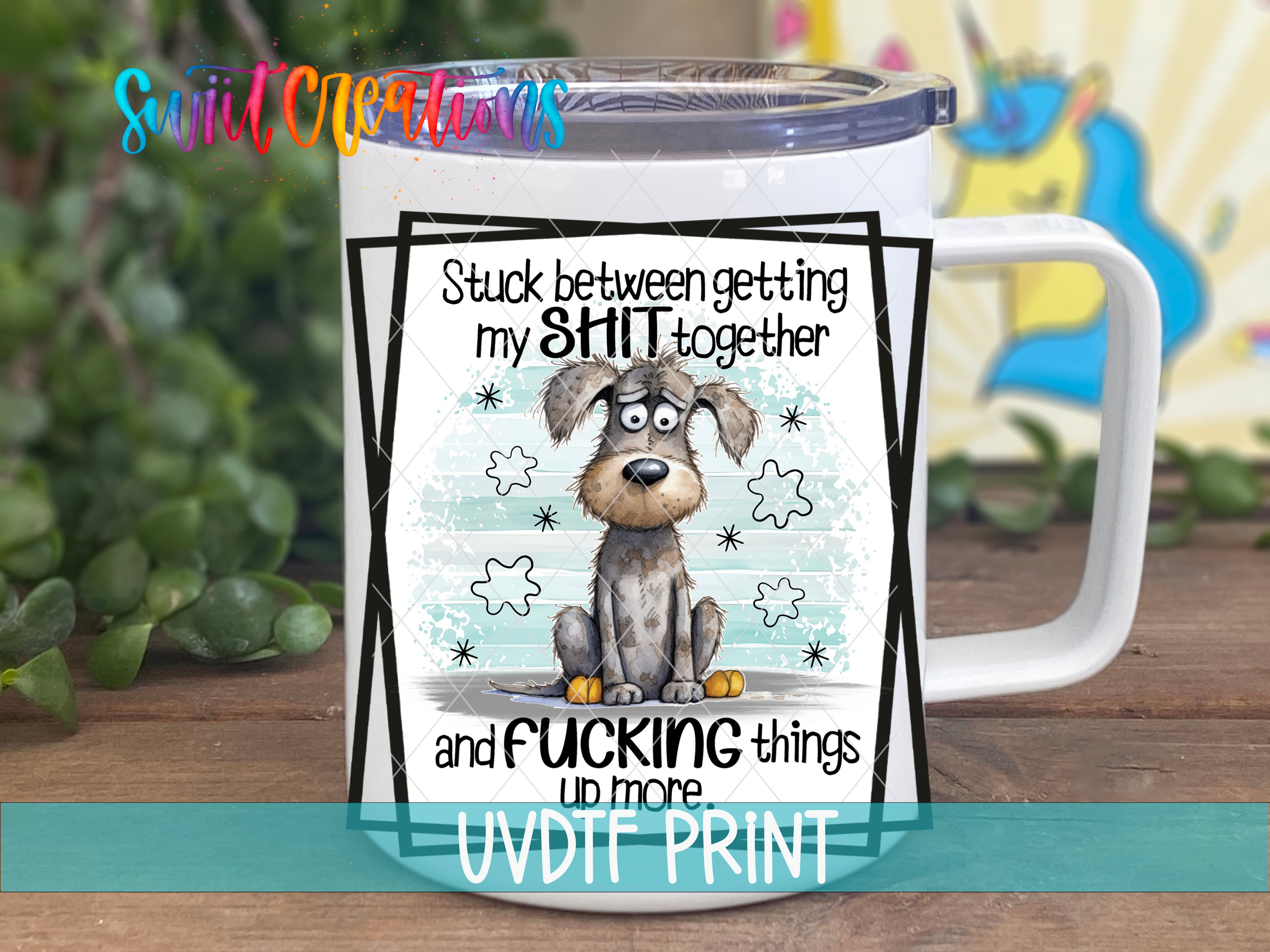 A mug with a humorous cartoon dog and text that reads "Stuck between getting my SHIT together and Fucking things up more", along with a colorful background.