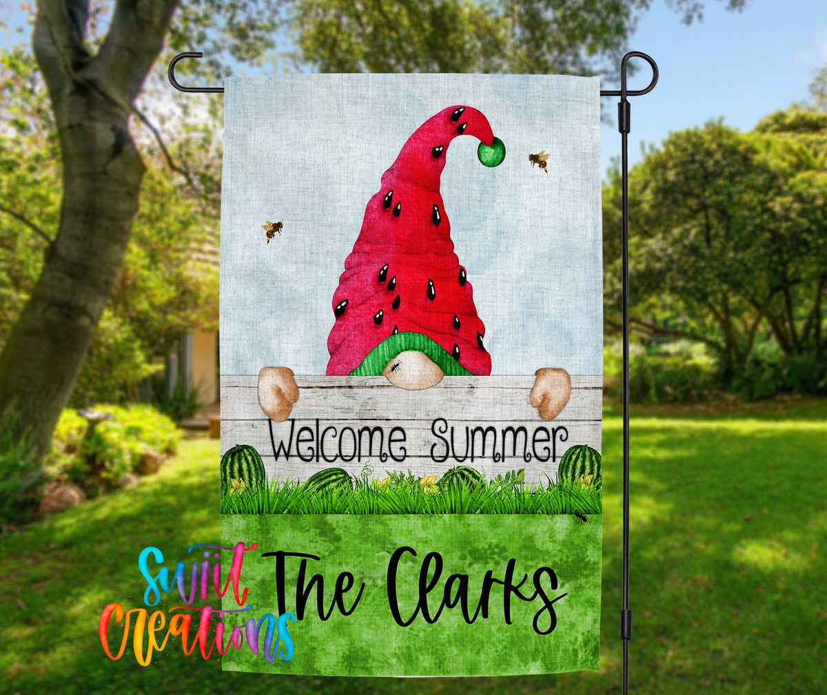 A garden gnome wearing a red hat with a green ball on top, standing behind a wooden fence and holding a sign that says "Welcome Summer".