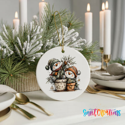 A white ceramic ornament featuring two snowmen is displayed on a table, surrounded by candles, greenery, and other holiday decor.