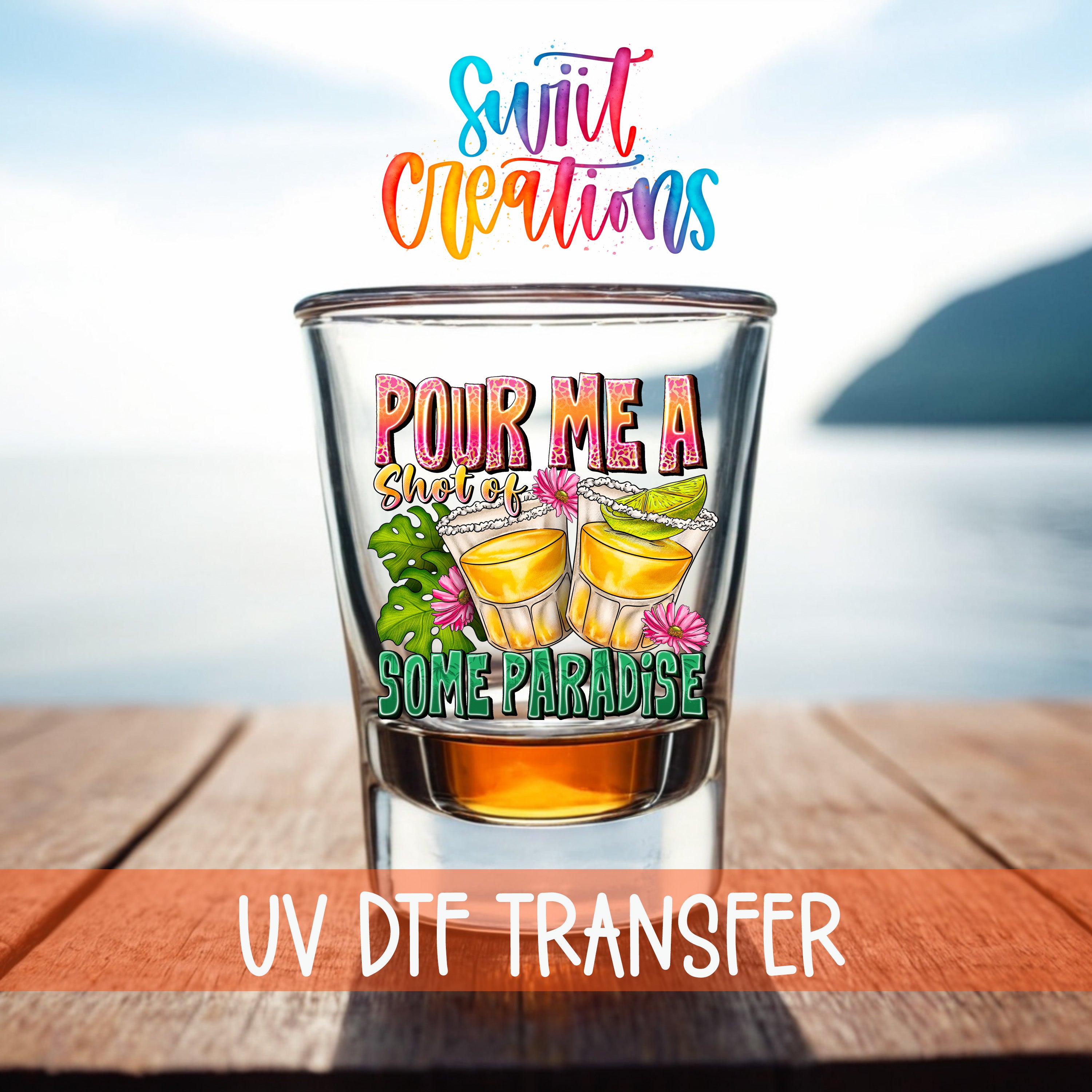 a shot glass with a colorful design and text, placed on a wooden surface with a body of water in the background.