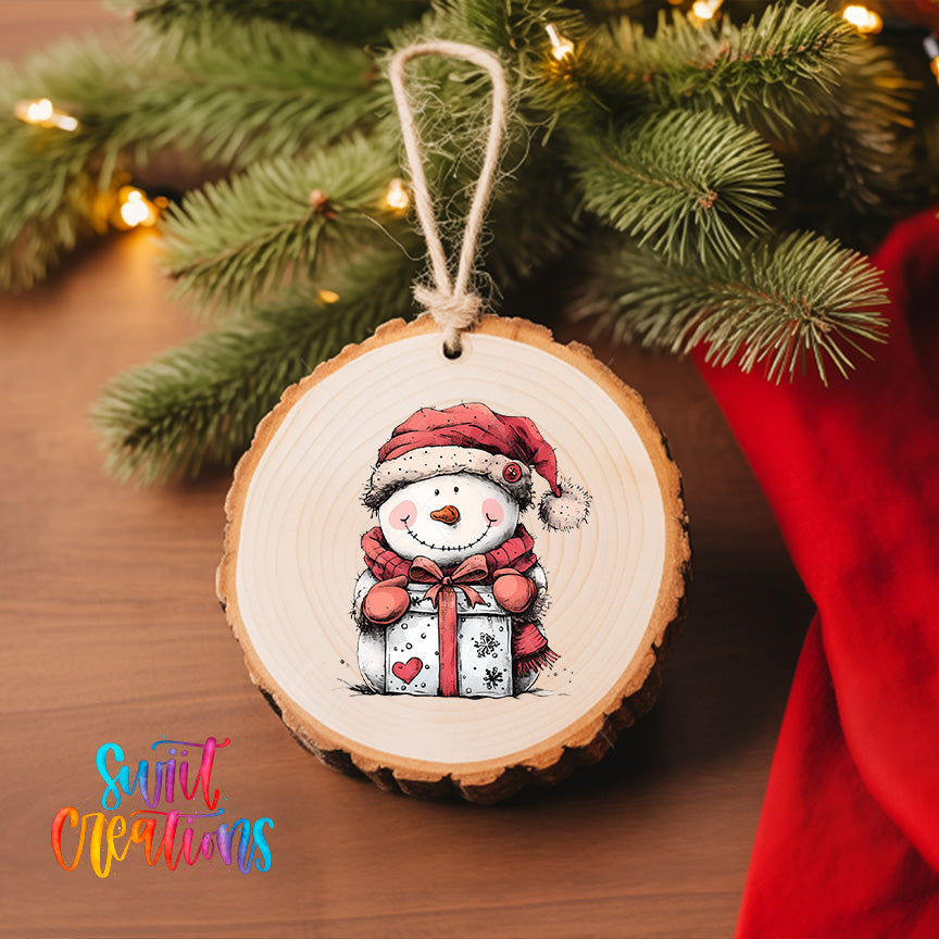 A wooden ornament featuring a smiling snowman holding a gift, hanging on a Christmas tree.