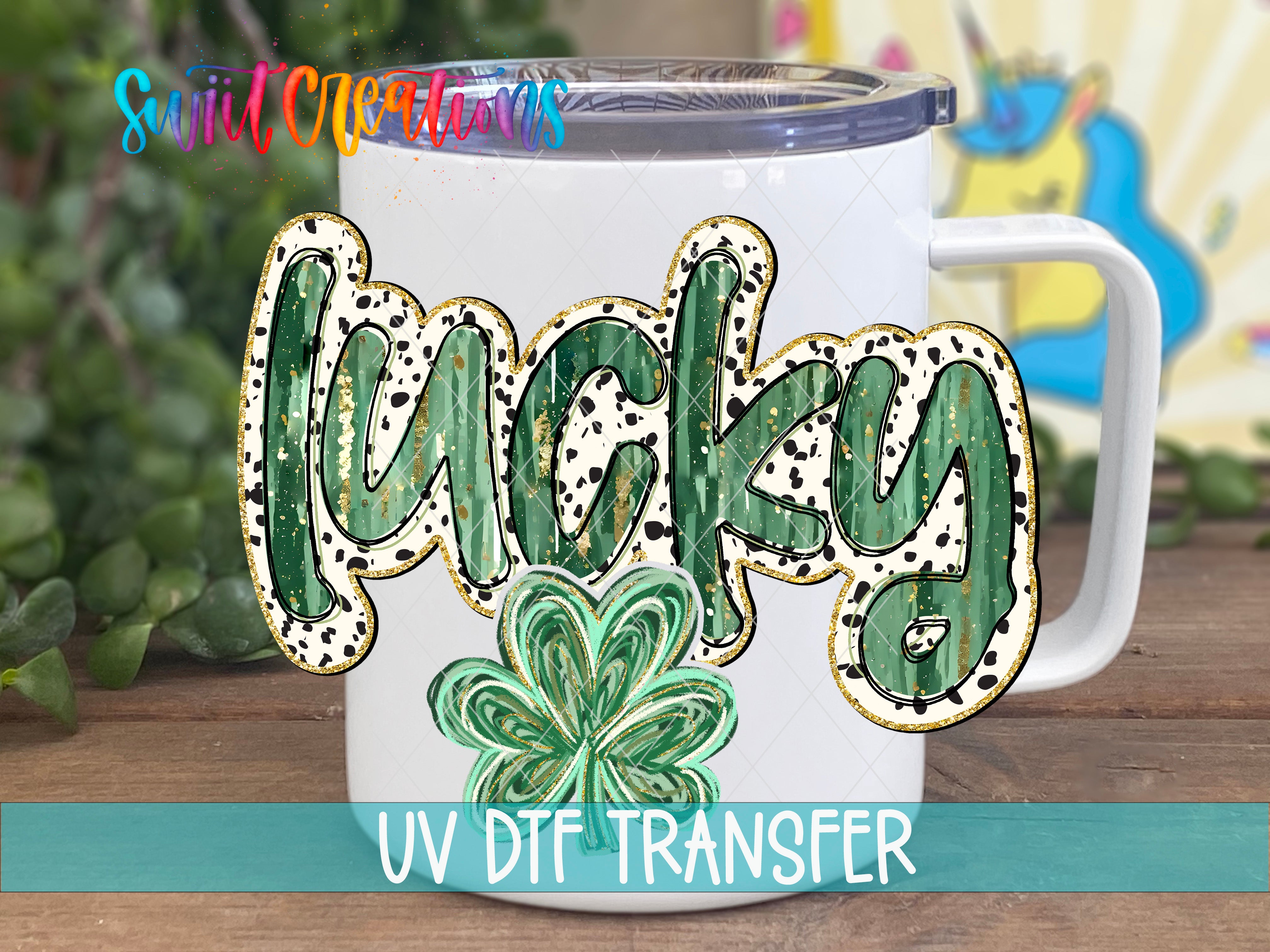 A white mug with the word "Lucky" written on it, along with a clover design. The mug is placed on a wooden surface, and there is a colorful background behind it.