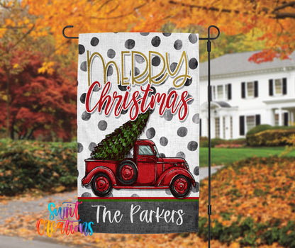 A white flag with a red truck carrying a Christmas tree, with the text "Merry Christmas" and "The Parkers" printed on it. The background features a house and trees with autumn foliage.