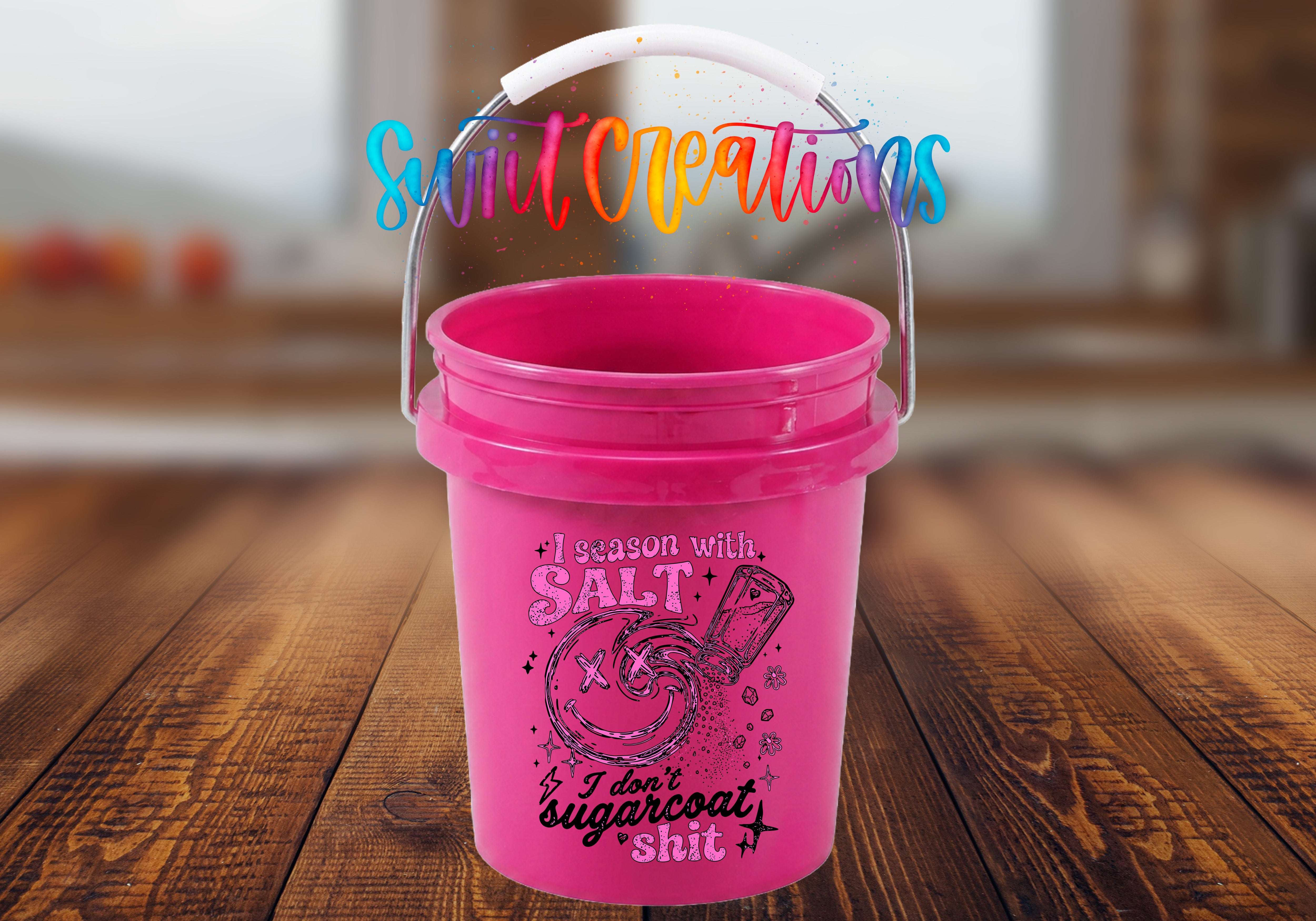 A pink bucket with a handle and a printed design on it, placed on a wooden surface.