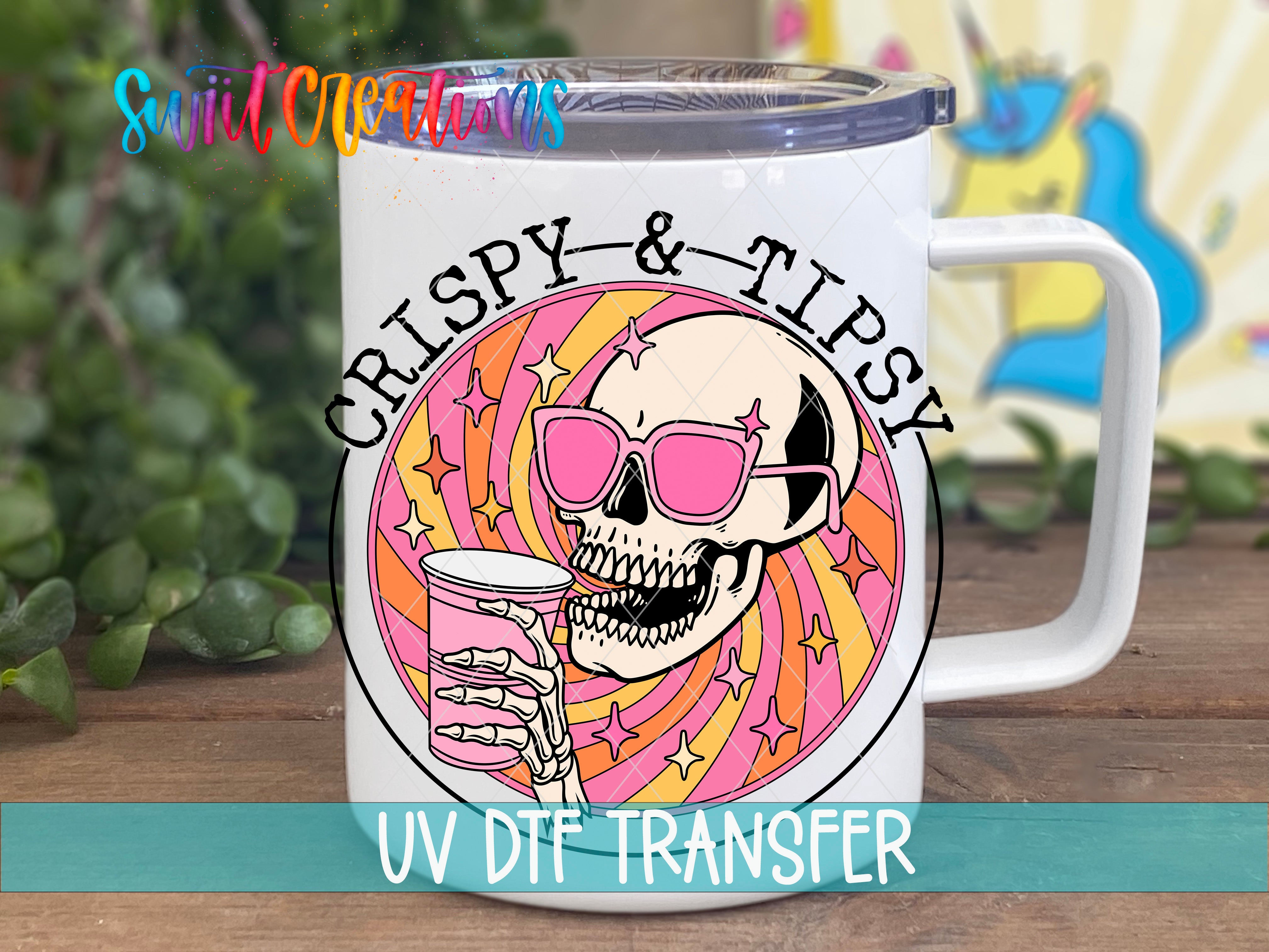 A white mug with a colorful design featuring a skull wearing sunglasses and holding a drink, with the text "CRISPY & TIPSY" and "UV DDF TRANSFER" printed on it.