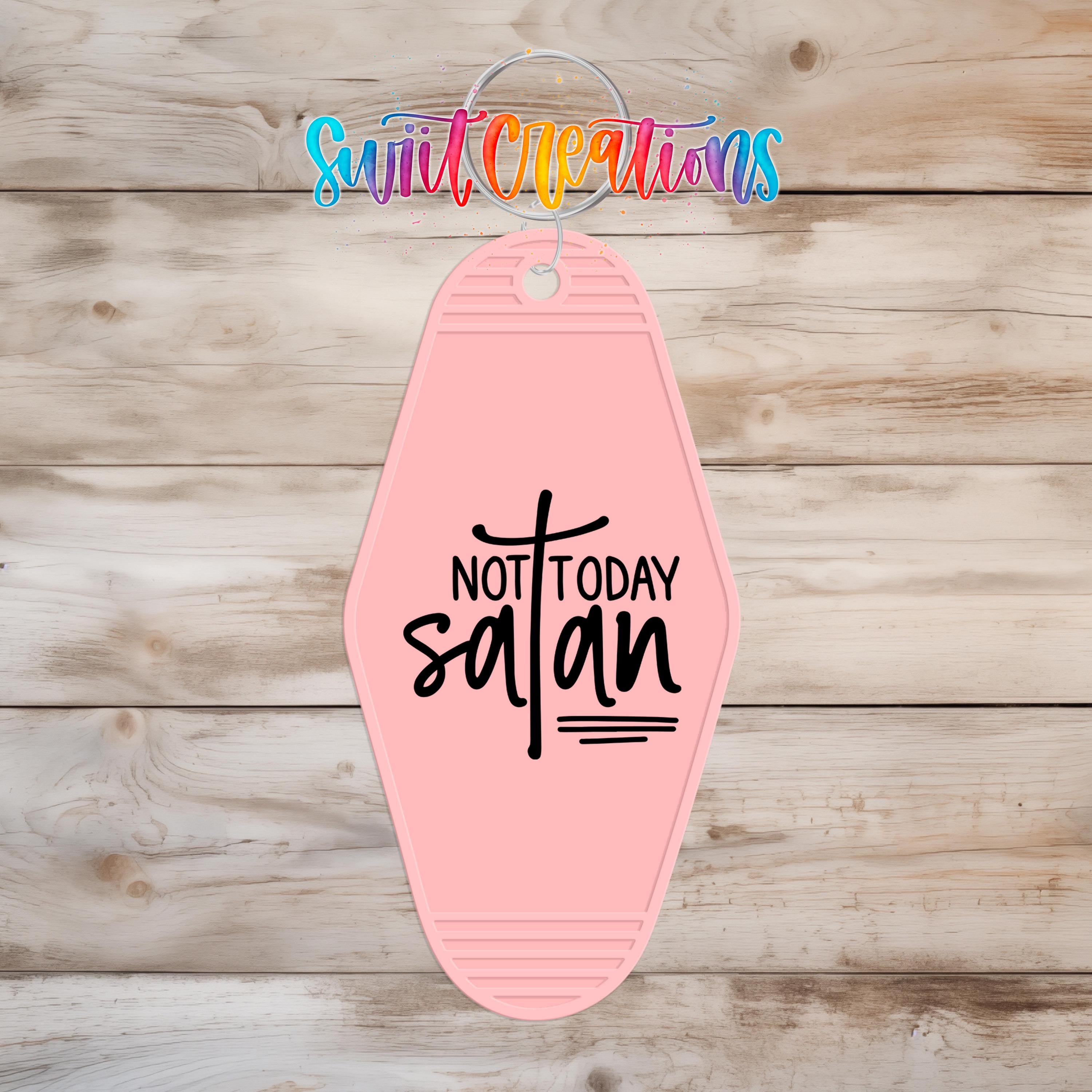 A pink keychain with the text "NOT TODAY SATAN" printed on it, hanging on a wooden surface.