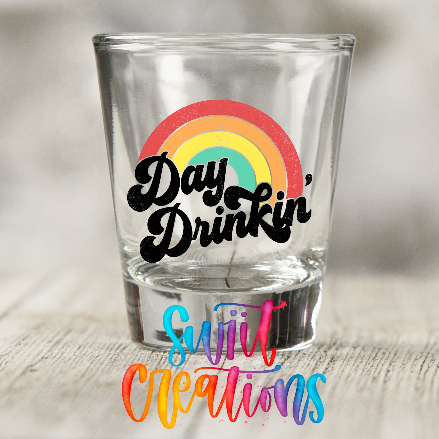 A clear shot glass with a colorful rainbow graphic and the text "Day Drinking" printed on it.