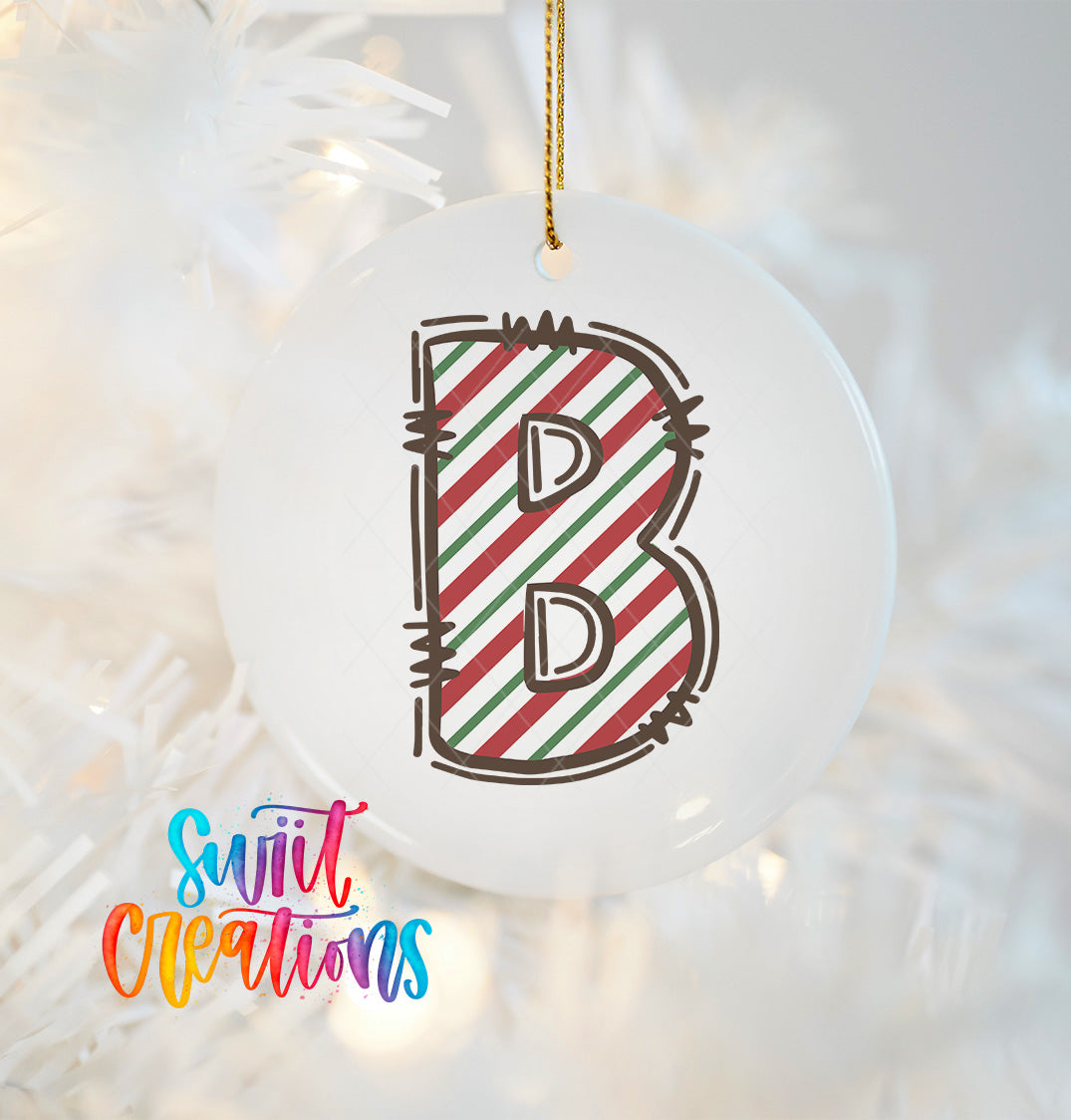 A white ornament with a large letter "B" in a striped design, hanging on a Christmas tree.