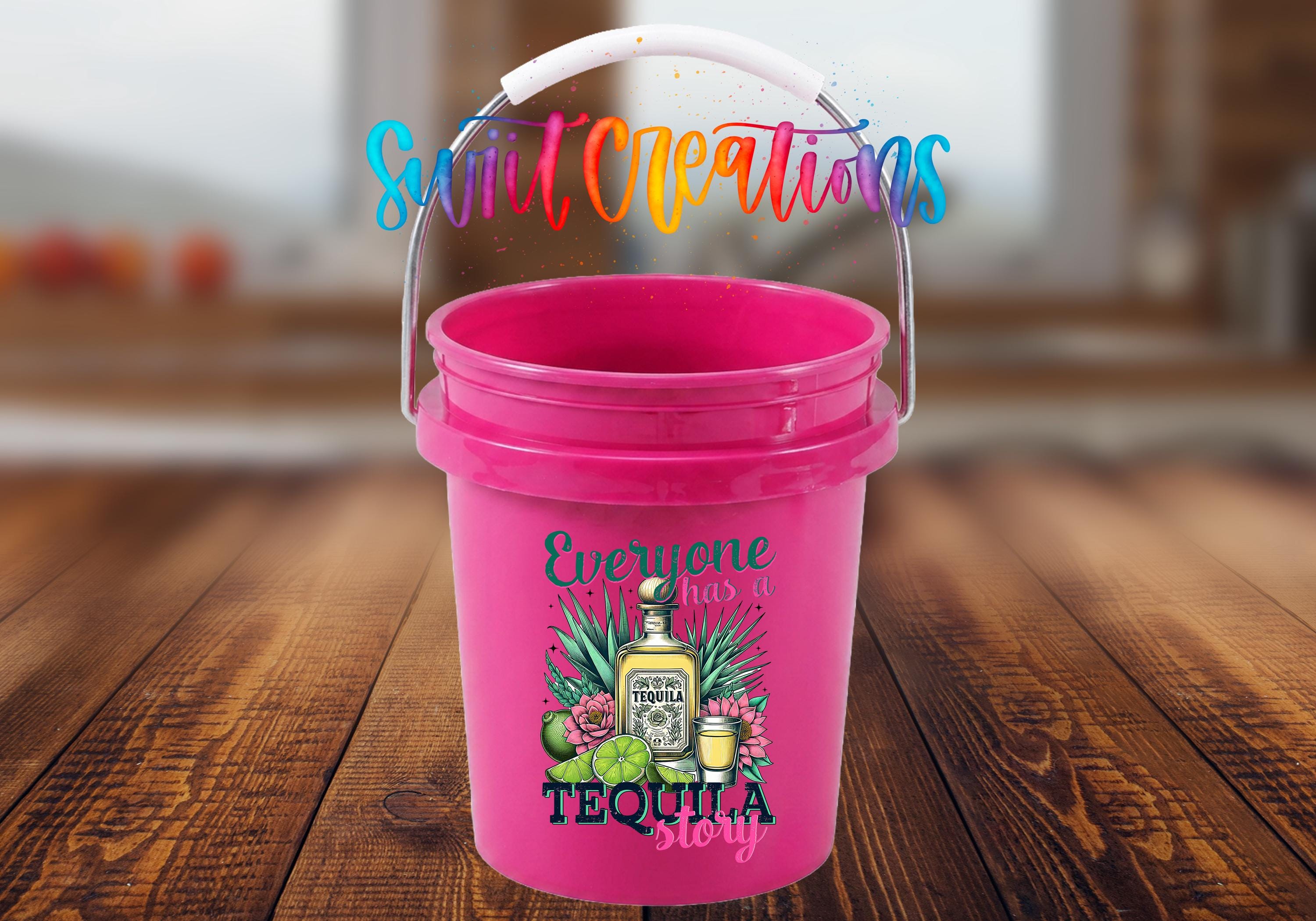 A pink bucket with a printed design of tequila bottles and a tequila bottle, along with the text "Everyone has a tequila story" and a colorful, rainbow-colored text above it.