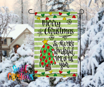 A festive Christmas-themed flag is displayed in a snowy outdoor setting, featuring a tree with red and green ornaments and a star on top.