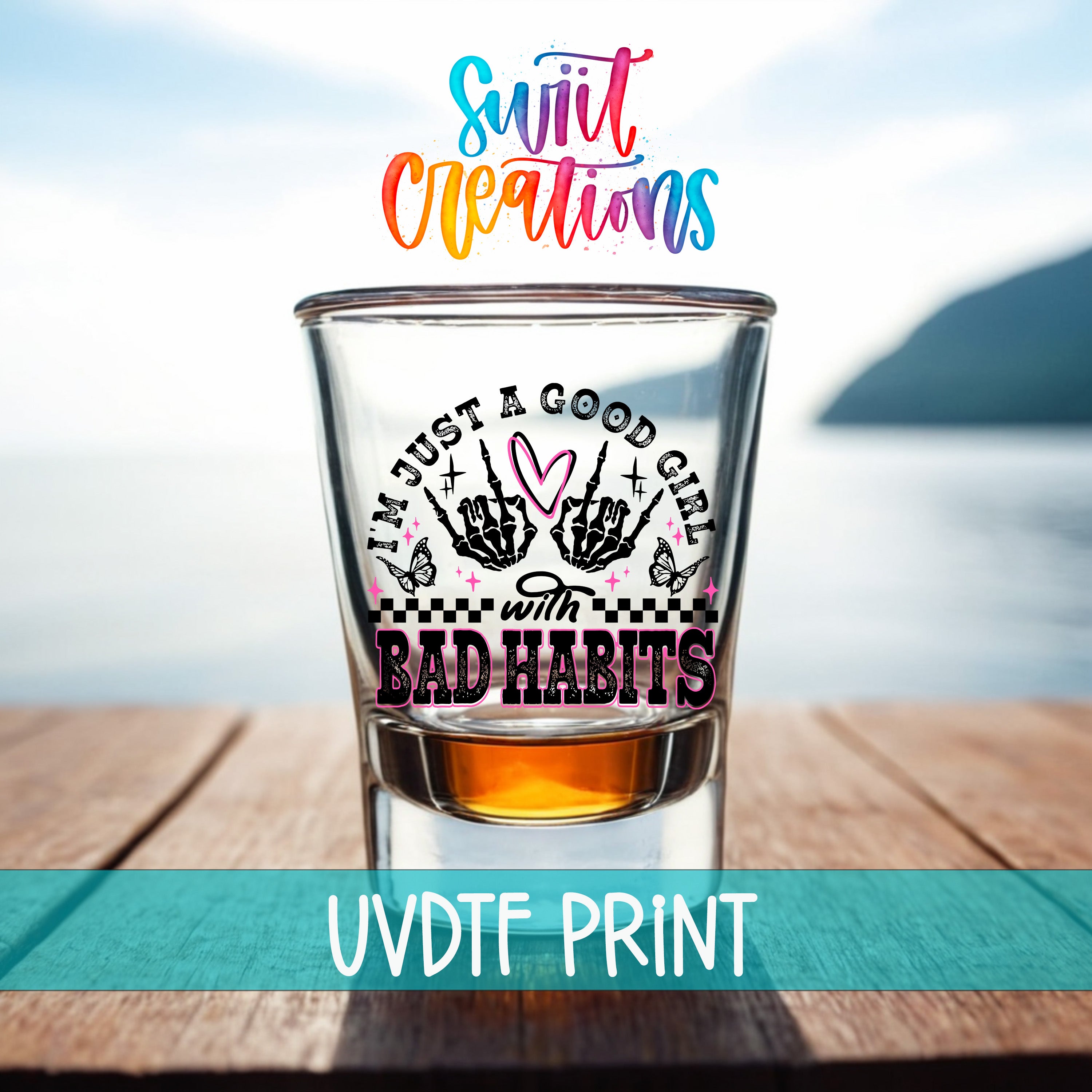 a shot glass with a colorful and artistic design, placed on a wooden surface with a body of water in the background.