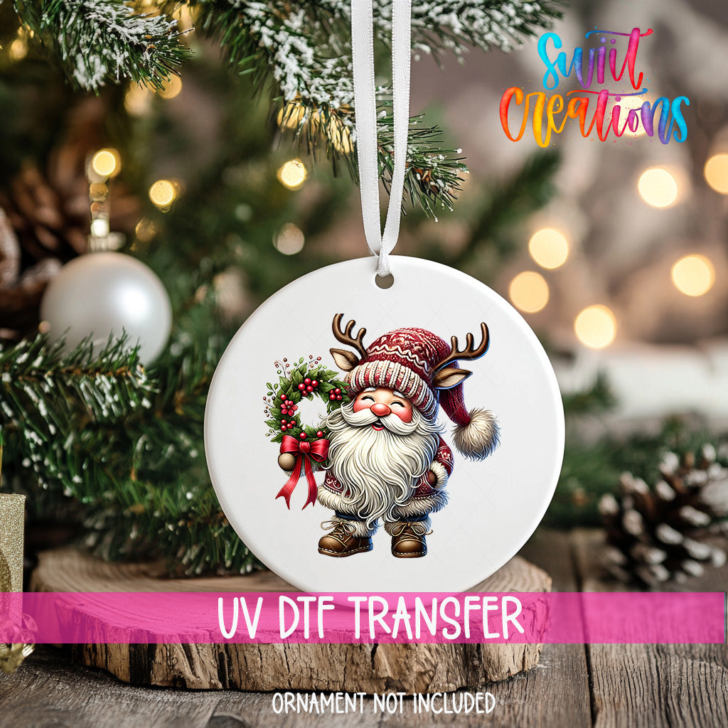 A white ornament with a Santa Claus figure and a wreath hangs on a Christmas tree.