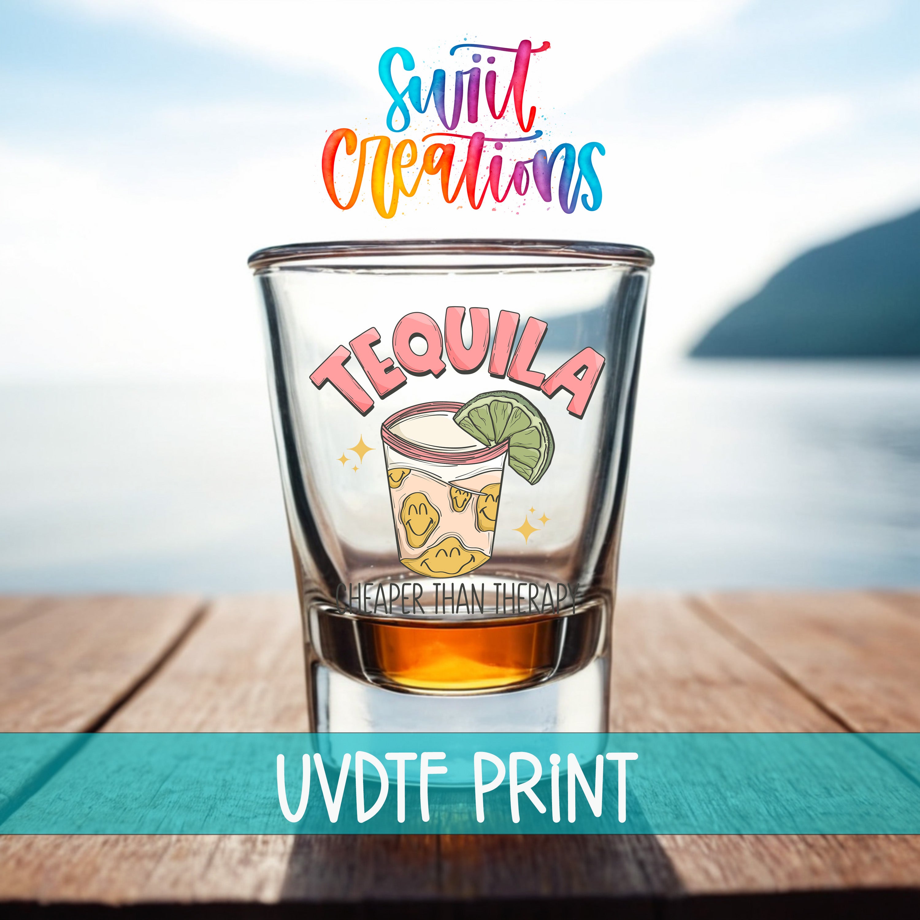 A shot glass with a tequila graphic and the text "HEAPER THAN THERAPY" printed on it, placed on a wooden surface with a body of water in the background.