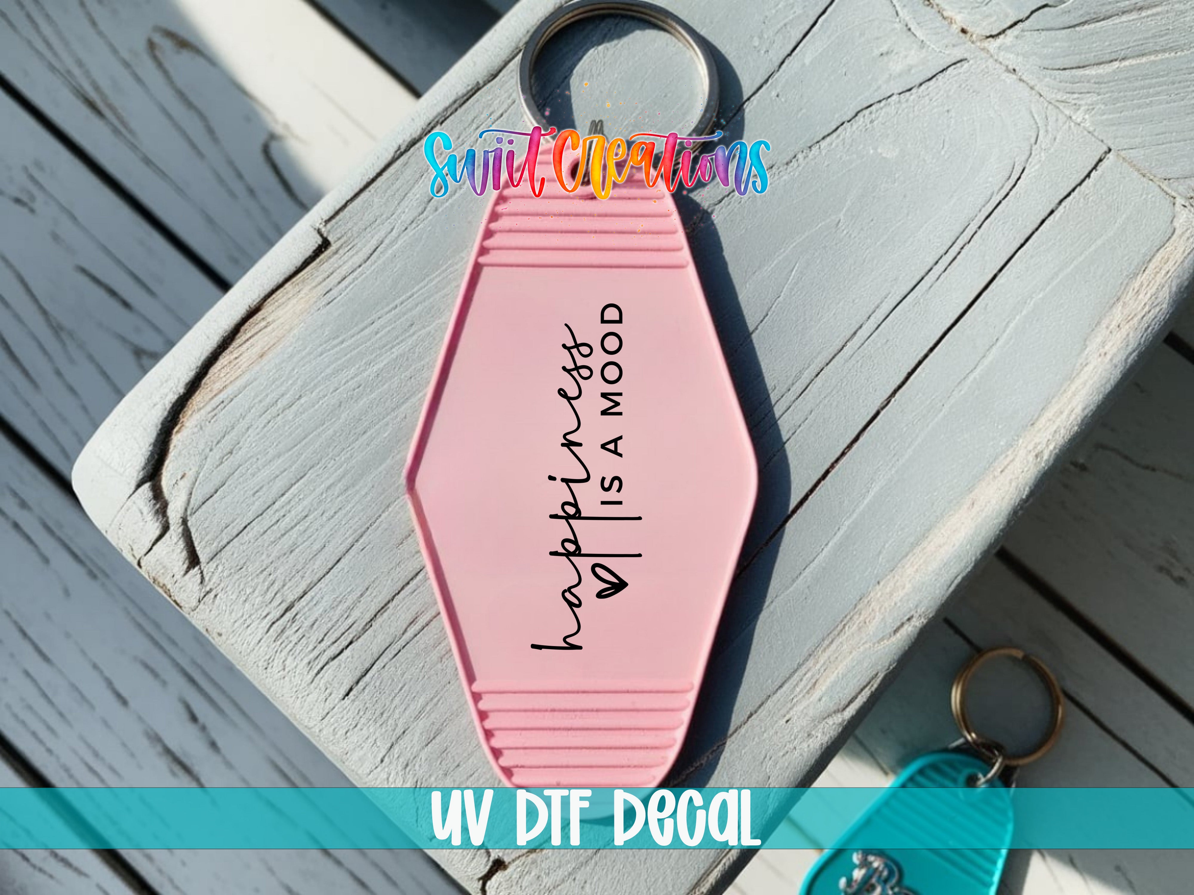 A pink keychain with the text "happiness is a mood" printed on it, placed on a wooden surface.
