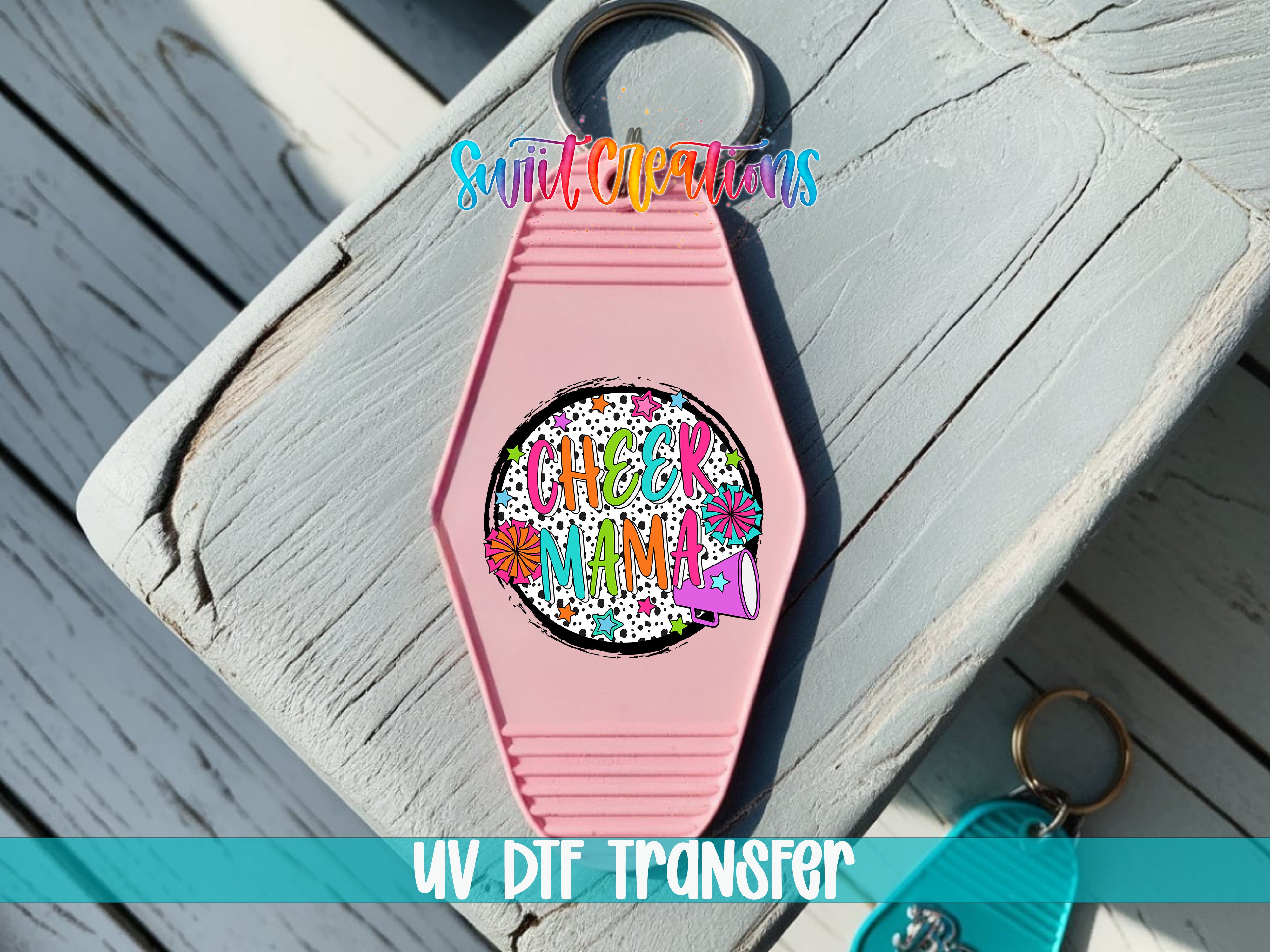 A pink keychain with a colorful design and text on it, placed on a wooden surface.