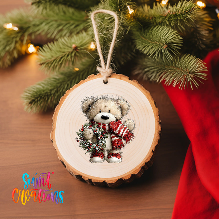 A wooden ornament featuring a teddy bear wearing a red scarf and holding a wreath, hanging on a Christmas tree.