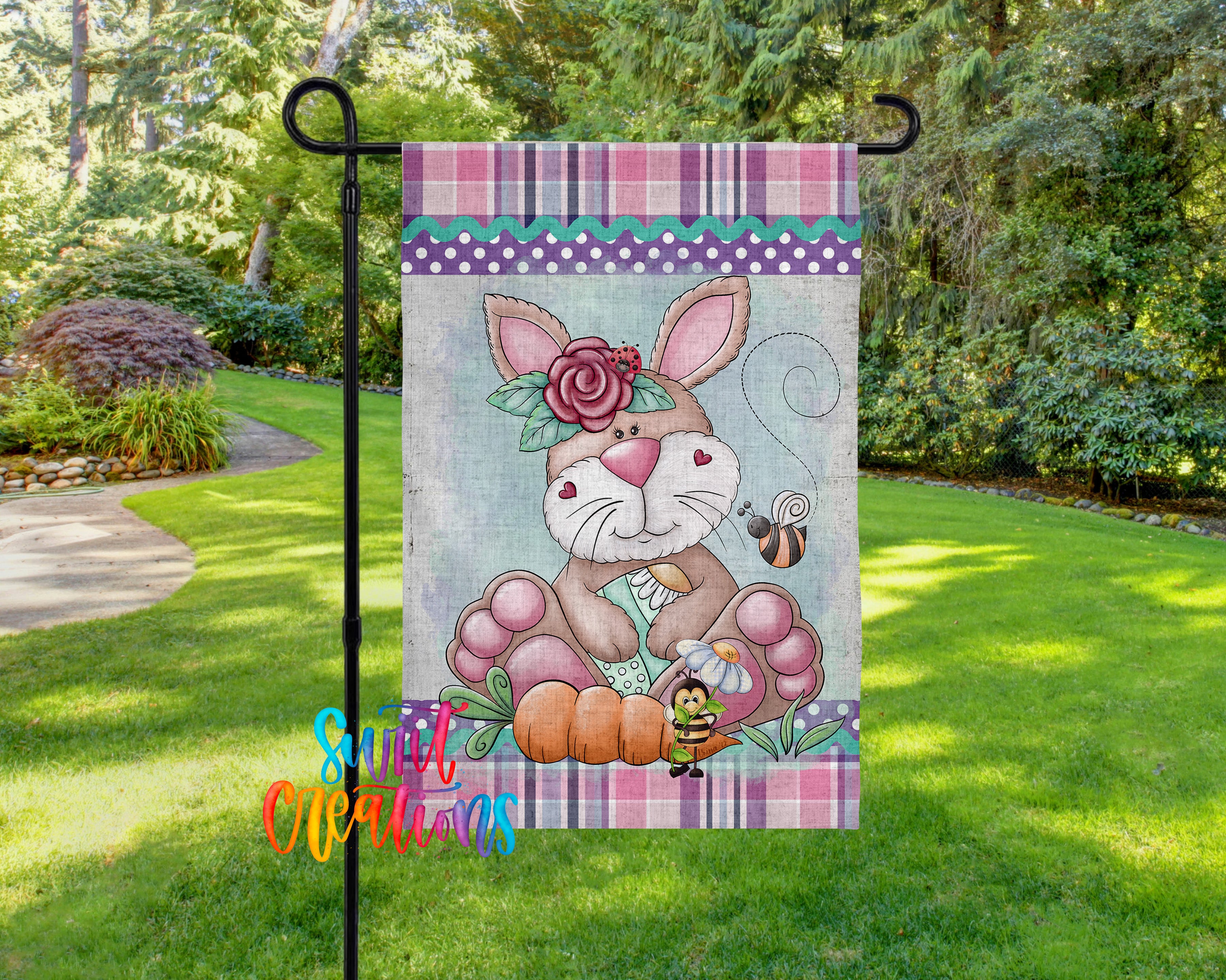 A colorful garden flag featuring a cartoon rabbit and a bee, with a floral border and a plaid pattern.