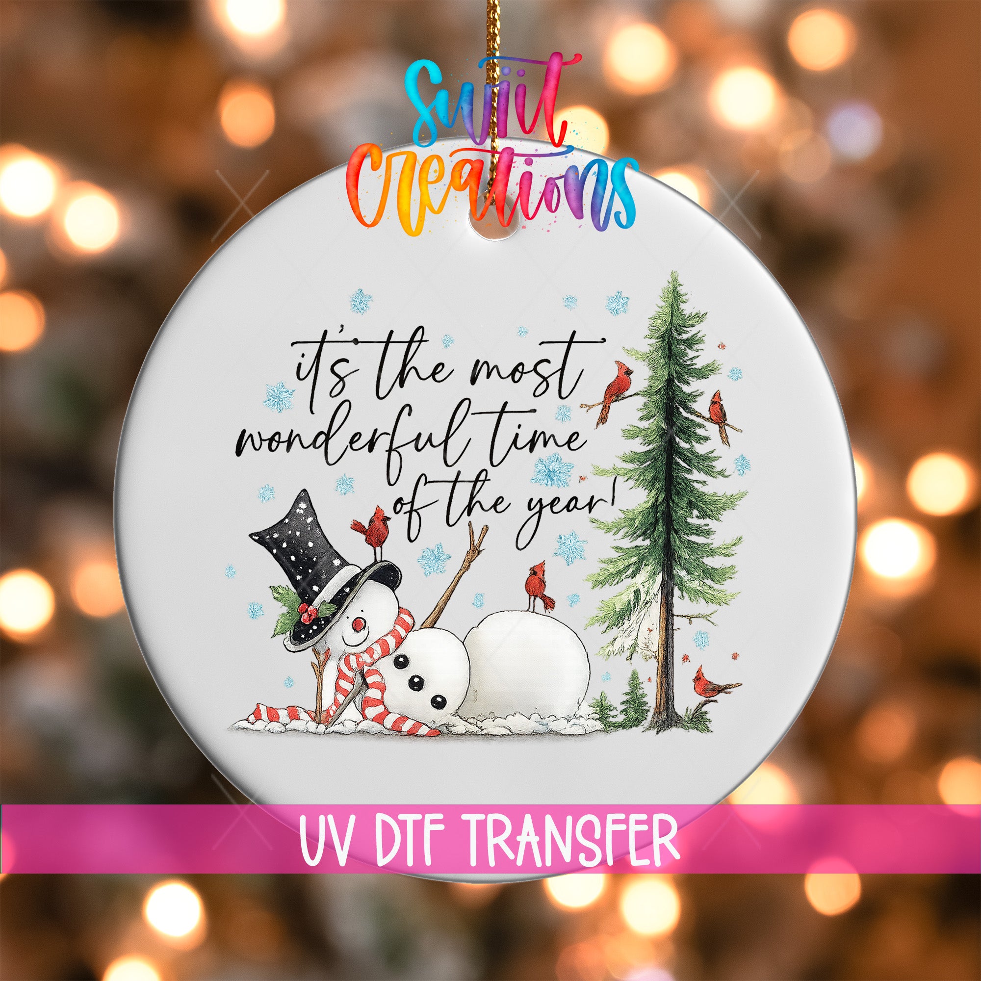 A white ornament with a snowman, a pine tree, and birds, along with a message that says "It's the most wonderful time of the year!" The ornament is hanging against a background with colorful lights.