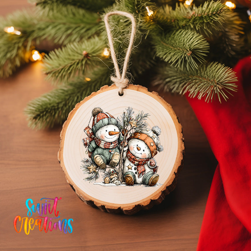 A wooden ornament featuring two snowmen is hanging on a Christmas tree, surrounded by pine branches and twinkling lights.