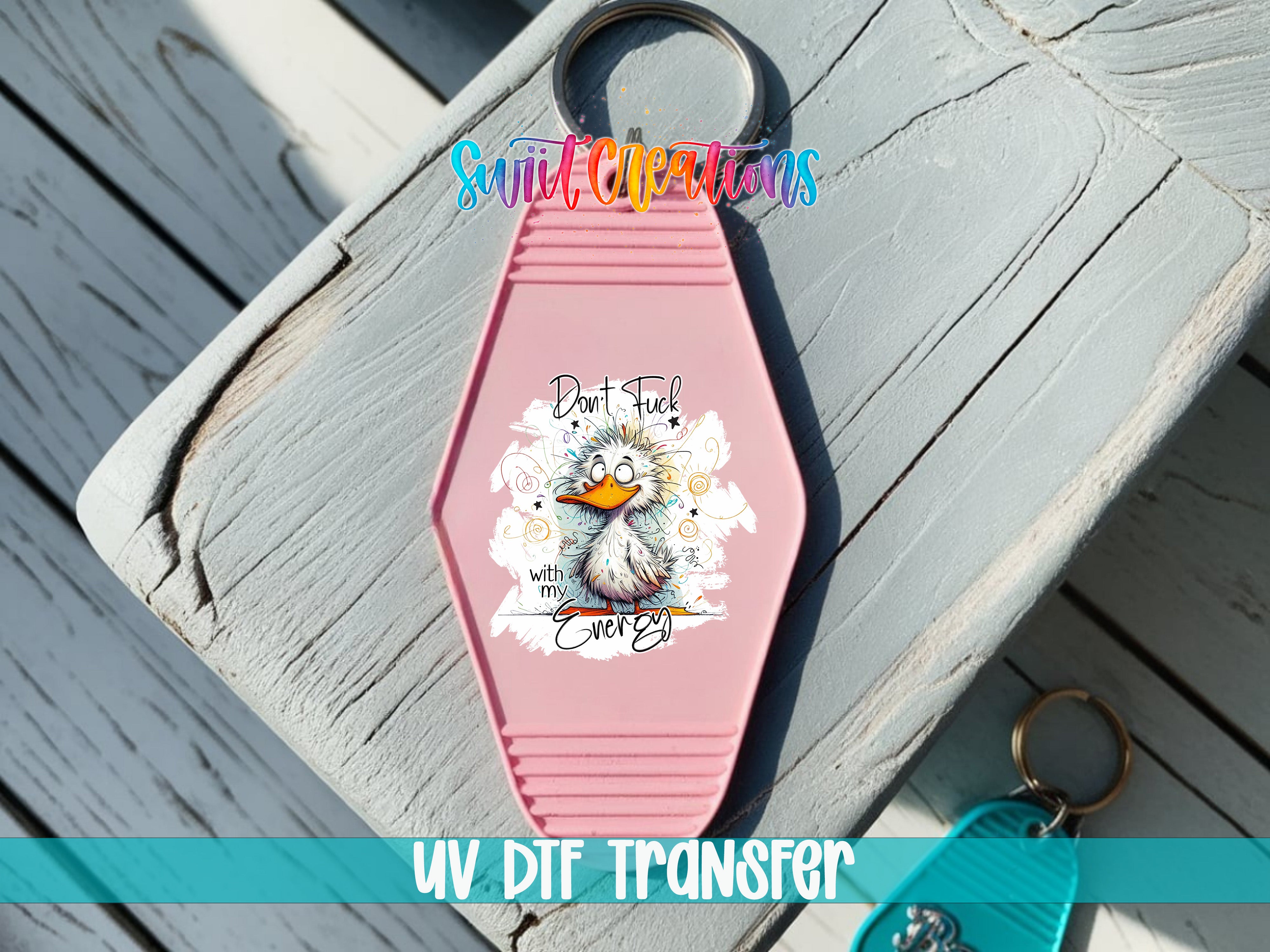 A pink keychain with a cartoon duck and the text "Don't F**k with your egg" printed on it, placed on a wooden surface.