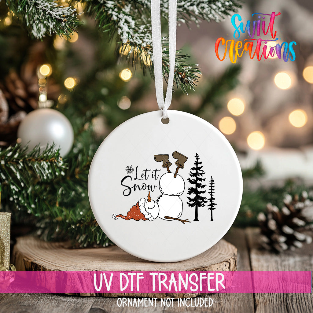 A white ceramic ornament with a snowman and the text "Let it Snow" is hanging on a Christmas tree.